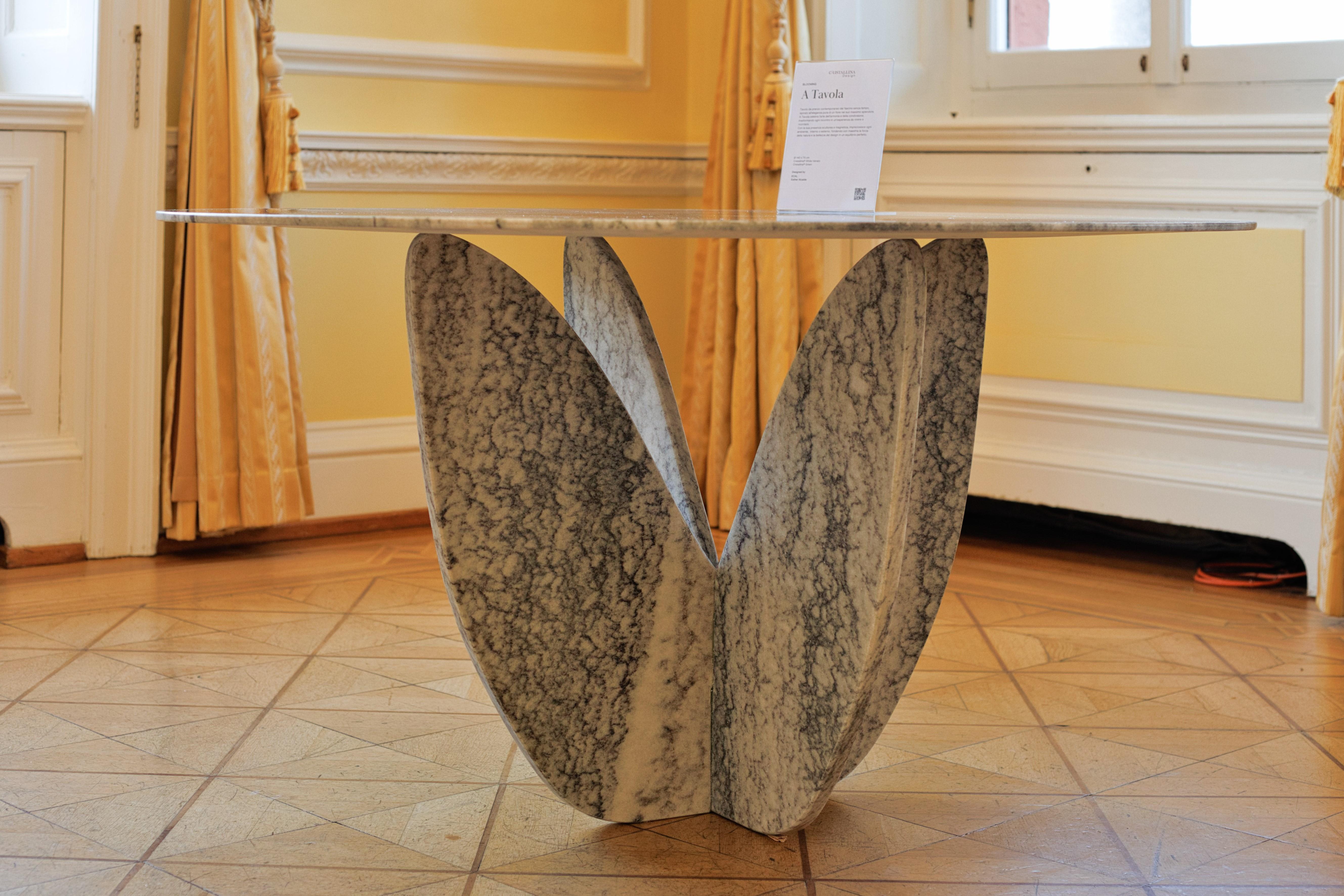 A Tavola es una mesa escultural de mármol Cristallina®, inspirada en la exuberante naturaleza de los jardines del Tesino. Su base sinuosa recuerda la forma de una flor en plena floración, símbolo de armonía y belleza atemporal, transformando un