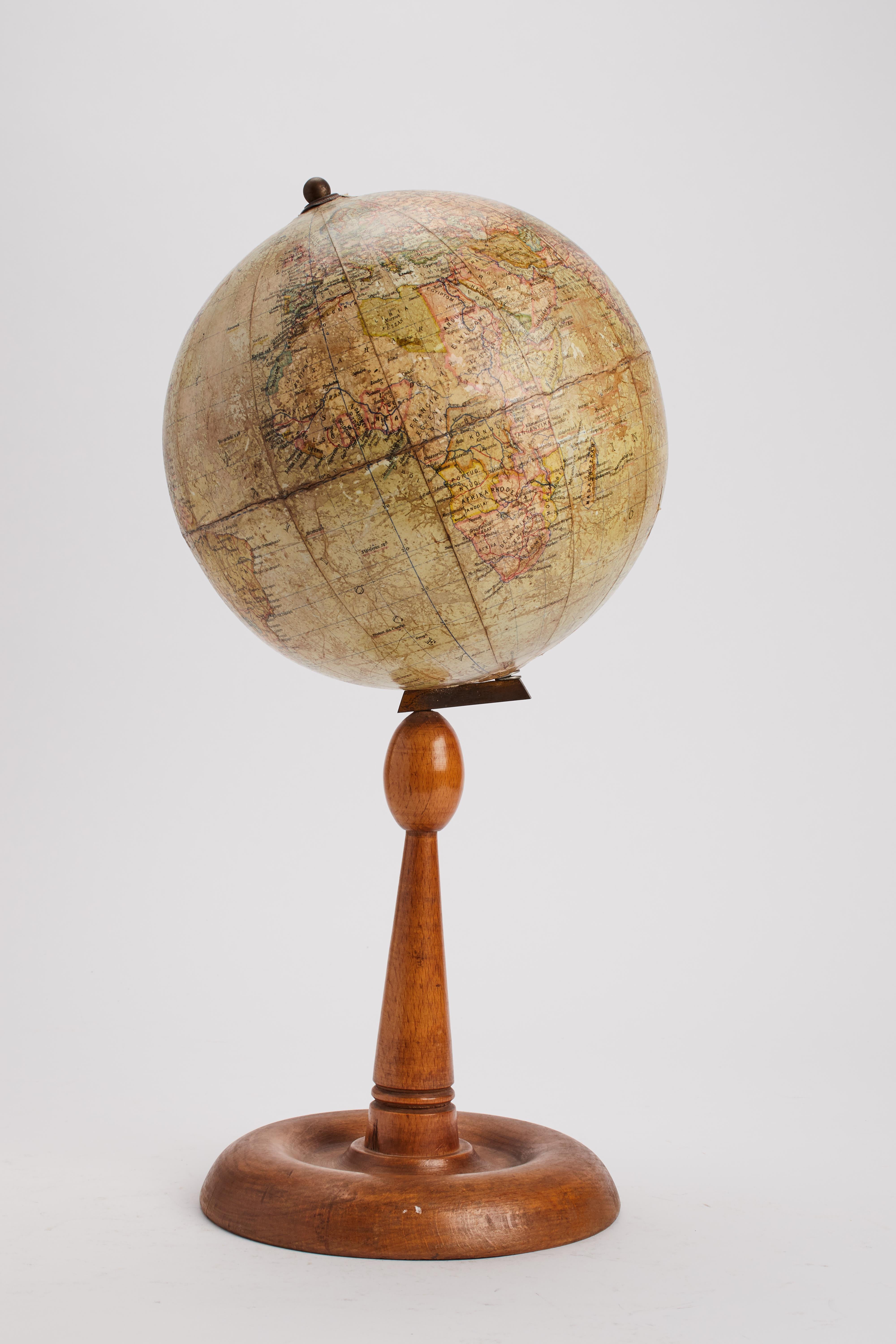 Medium-sized paper mache terrestrial globe on a turned maple wood base. The globe is tilted and connected to the base by a metal stand. Published by Földgömb. Budapest, Hungary circa 1920.