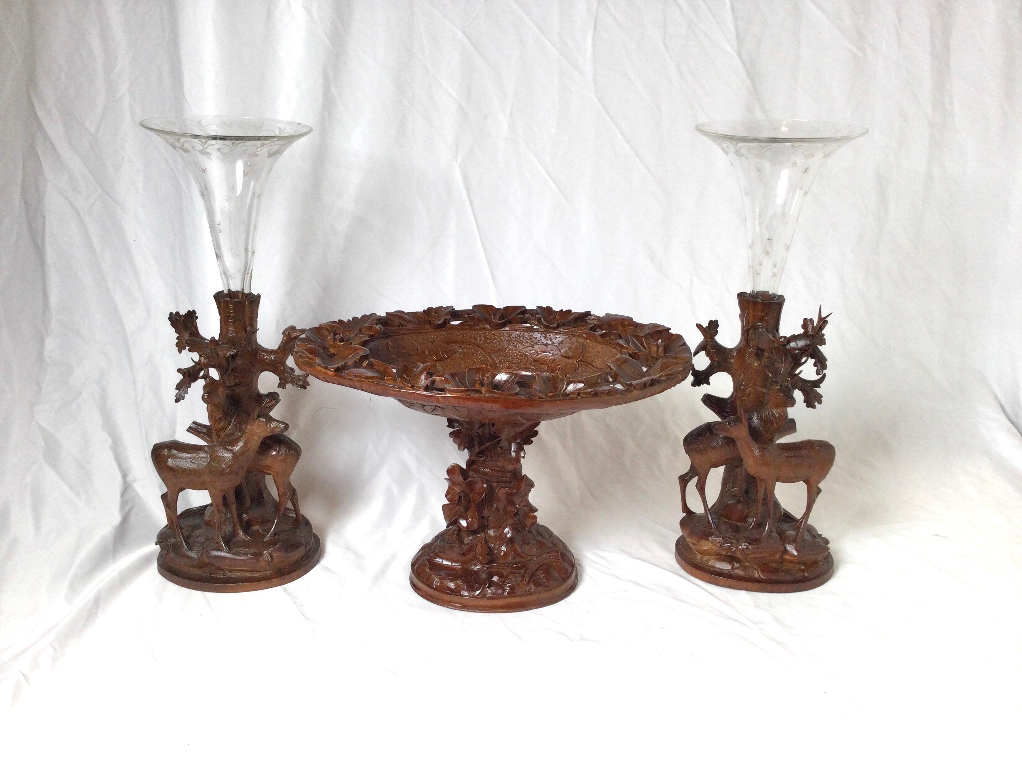 A three piece Black Forest set consisting of and oval pedestal center bow with two flanking wood and etched glass trumpet garniture. The set is a medium hand carved black forest Germany set, with beautiful etched glass trumpet inserts. small chip on