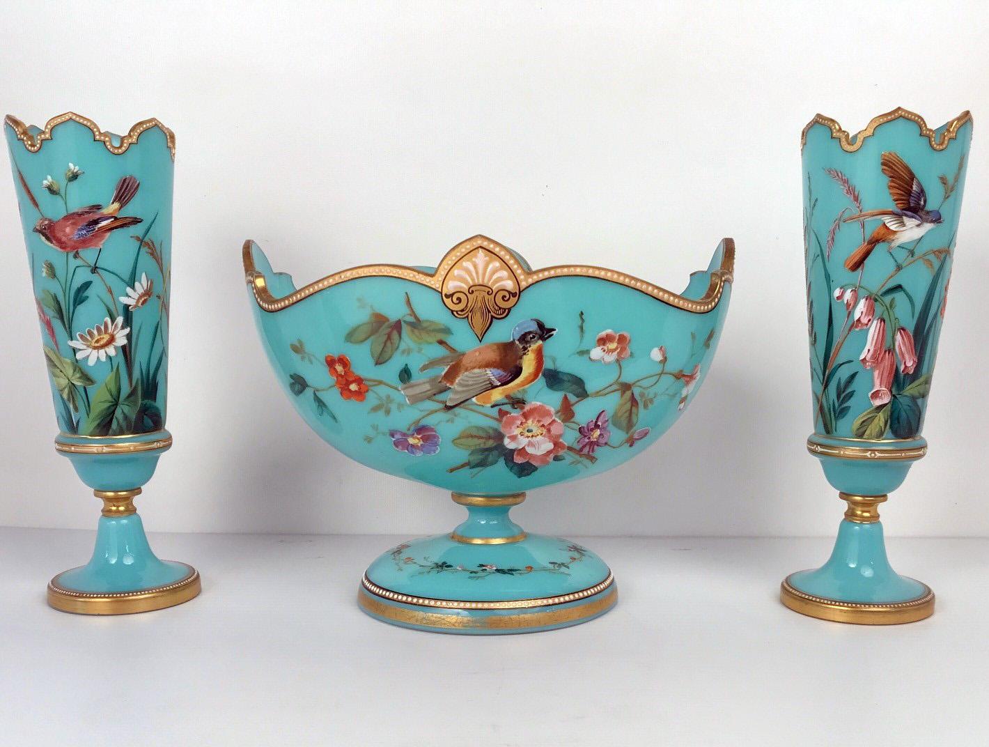 This garniture is painted with birds and flowers on a pale blue ground. The oblong footed bowl has a shaped gilt rim ,with white jewelling and centering palmettes. The flanking vases have crenellated rims and decoration that match the central