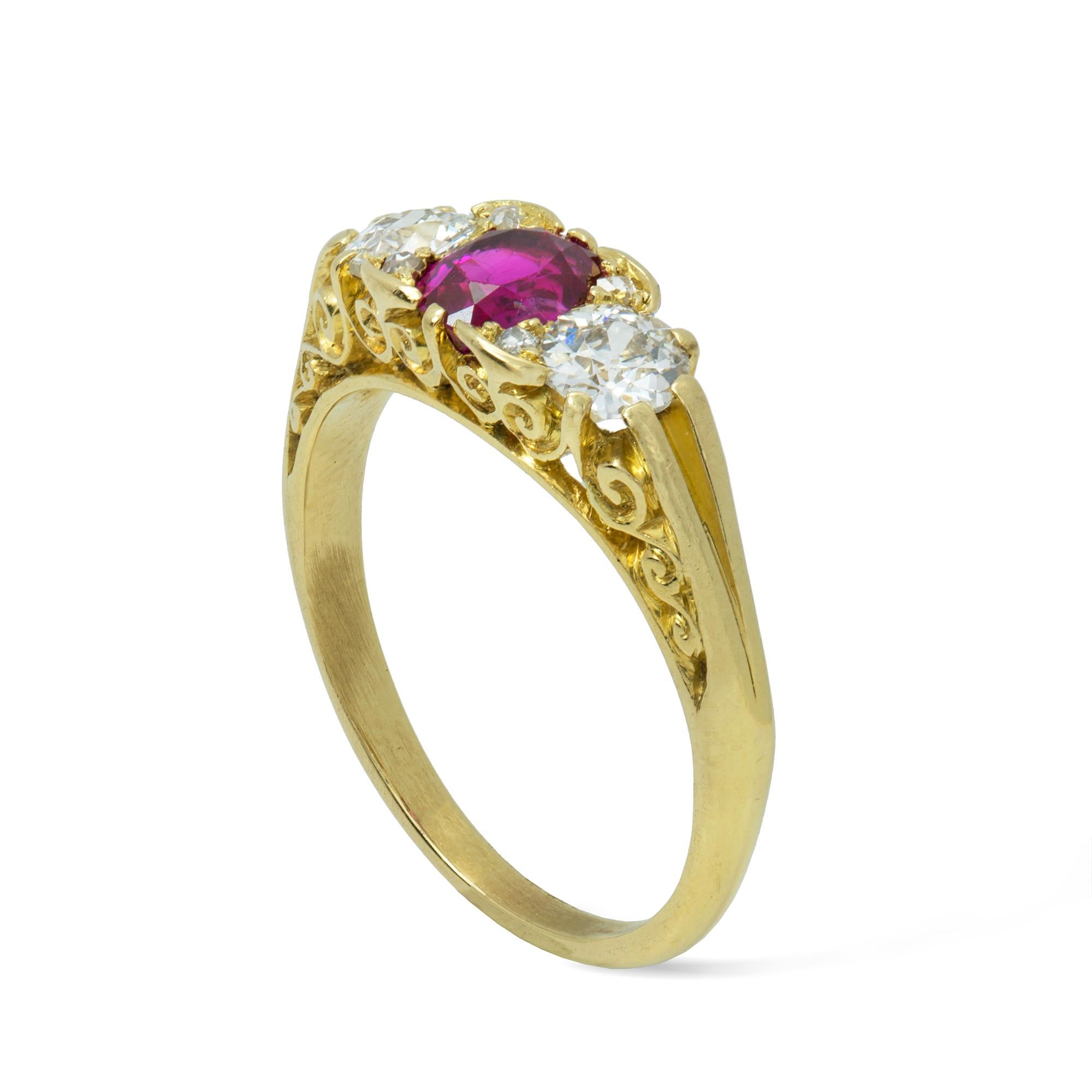 A three stone carved half loop ruby and diamond ring, the oval faceted ruby weighing an estimated 0.60 carats set between two old brilliant-cut diamonds weighing approximately 0.8 carats in total all to a scrolled pierced yellow gold mount,  circa