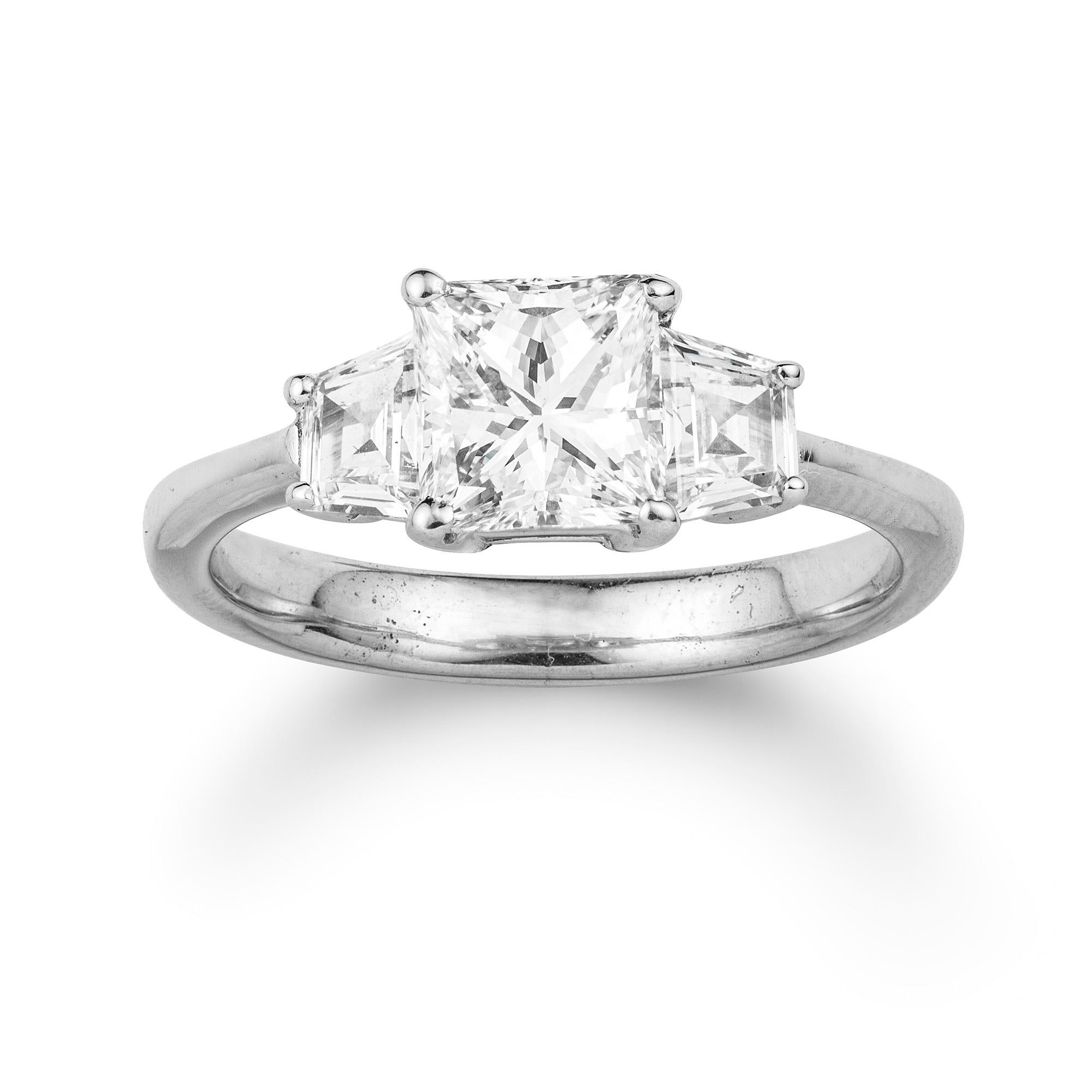 A three stone diamond ring, the centre a princess-cut diamond weighing 1.13 carats accompanied by GCS Report stating to be of H colour and VS1 clarity, claw-set between trapeze-cut diamond-set shoulders weighing a further total of 0.51 carats, to
