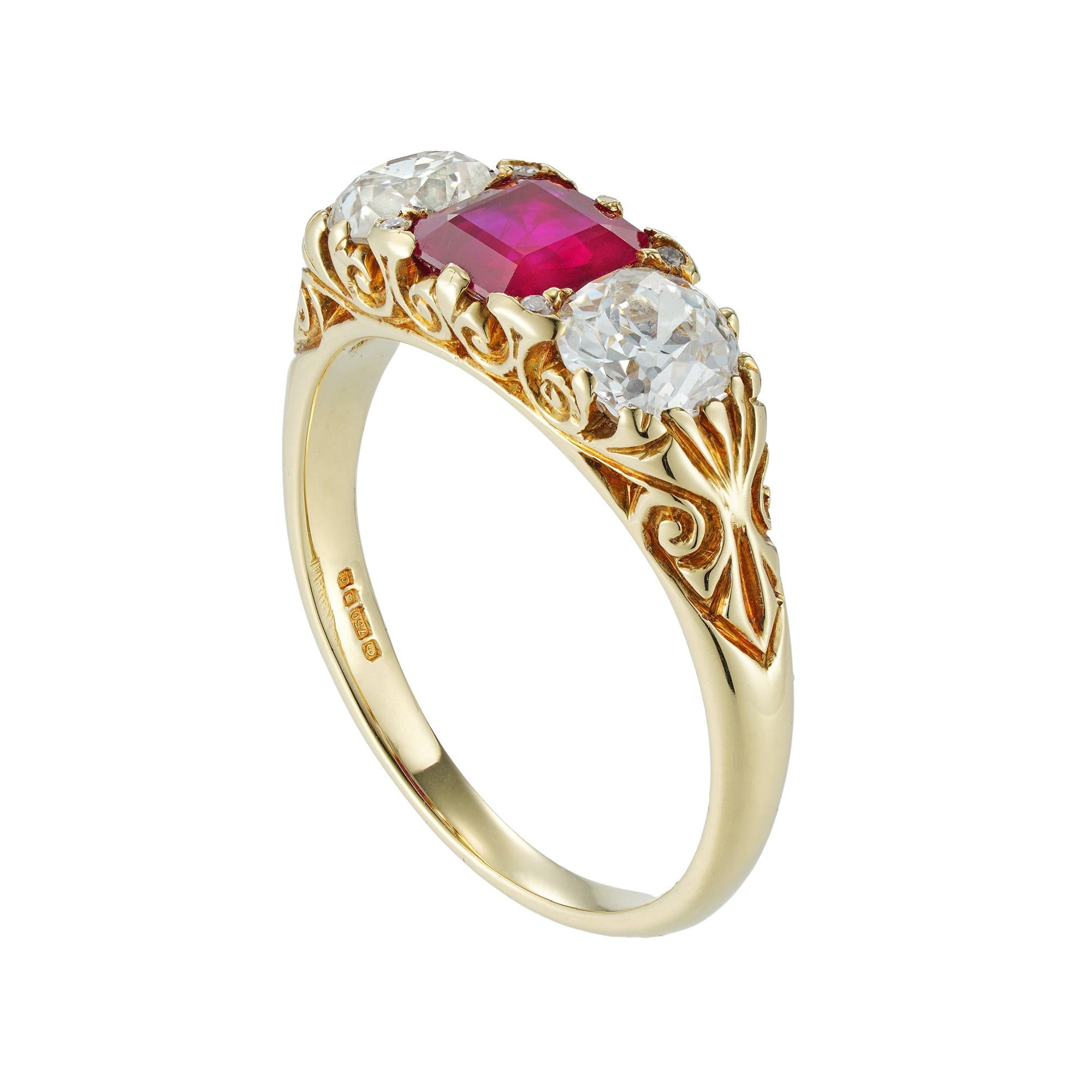 A three stone ruby and diamond carved half hoop ring, the central emerald-cut ruby weighing 0.85cts, accompanied by GCS Report stating to be of Burmese origin, set between two old-cut diamonds estimated to weigh a total of 1.10cts, all claw set to a