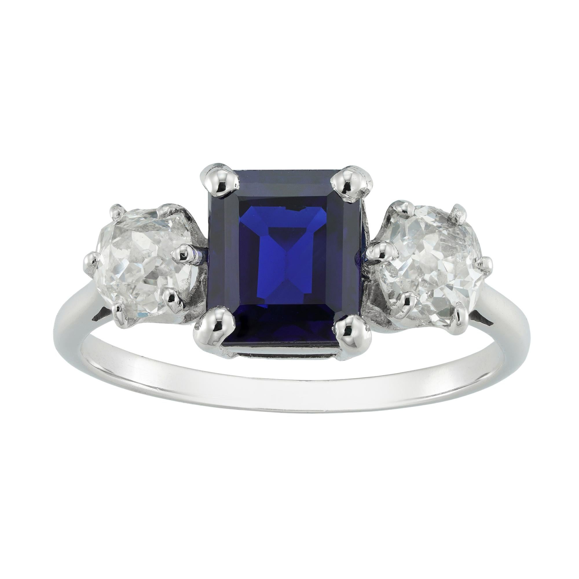 A three stone sapphire and diamond ring, the square-cut sapphire weighing 1.60 carats, accompanied by GCS report stating to be of basaltic origin with no indication of heating, set between two old-cut diamonds, the one weighing 0.32 carats and the