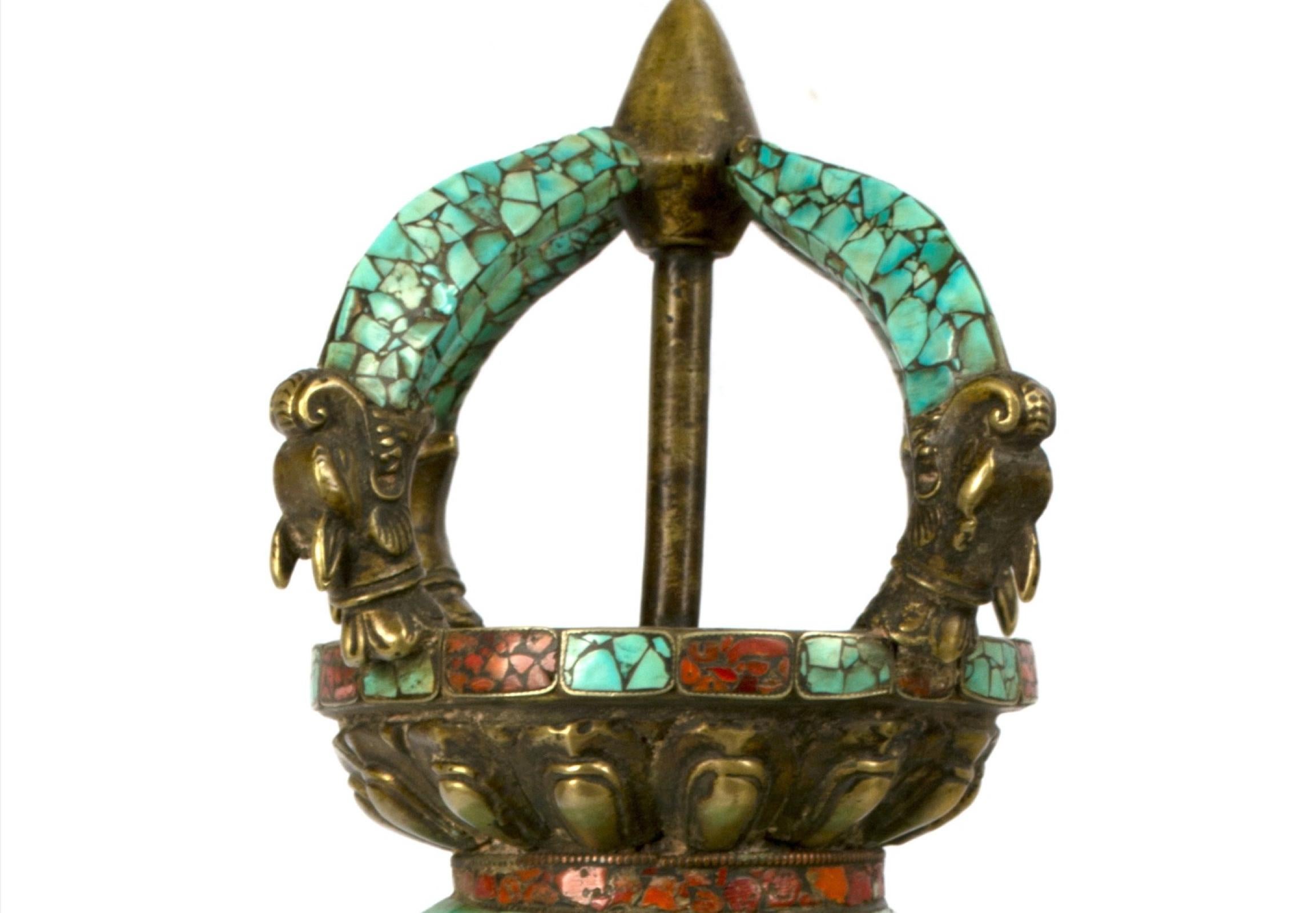 An unusual double vajra, a representation of both the diamond (indestructibility) and thunderbolt (heavenly power), covered in gilt bronze, turquoise and carnelian. The two vajras are united by a sphere (the world) and lotuses. The work is in