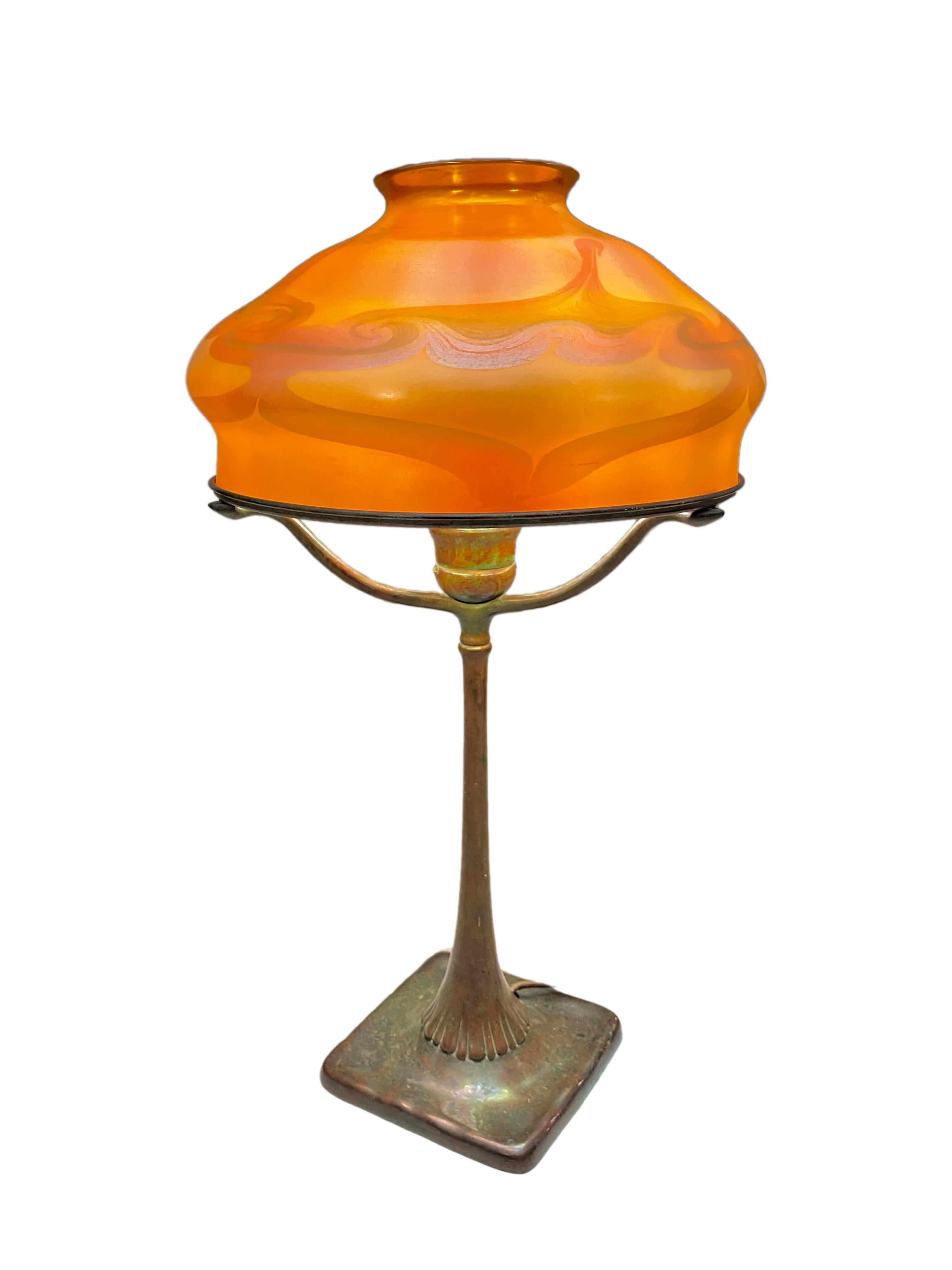 A Tiffany Favrile and bronze Art Nouveau desk lamp by, Tiffany Studios decorated with an early, reactive and heavily iridescent Tiffany Favrile art glass shade with iridescent purple-pink and green-yellow stylized pulled feather decoration