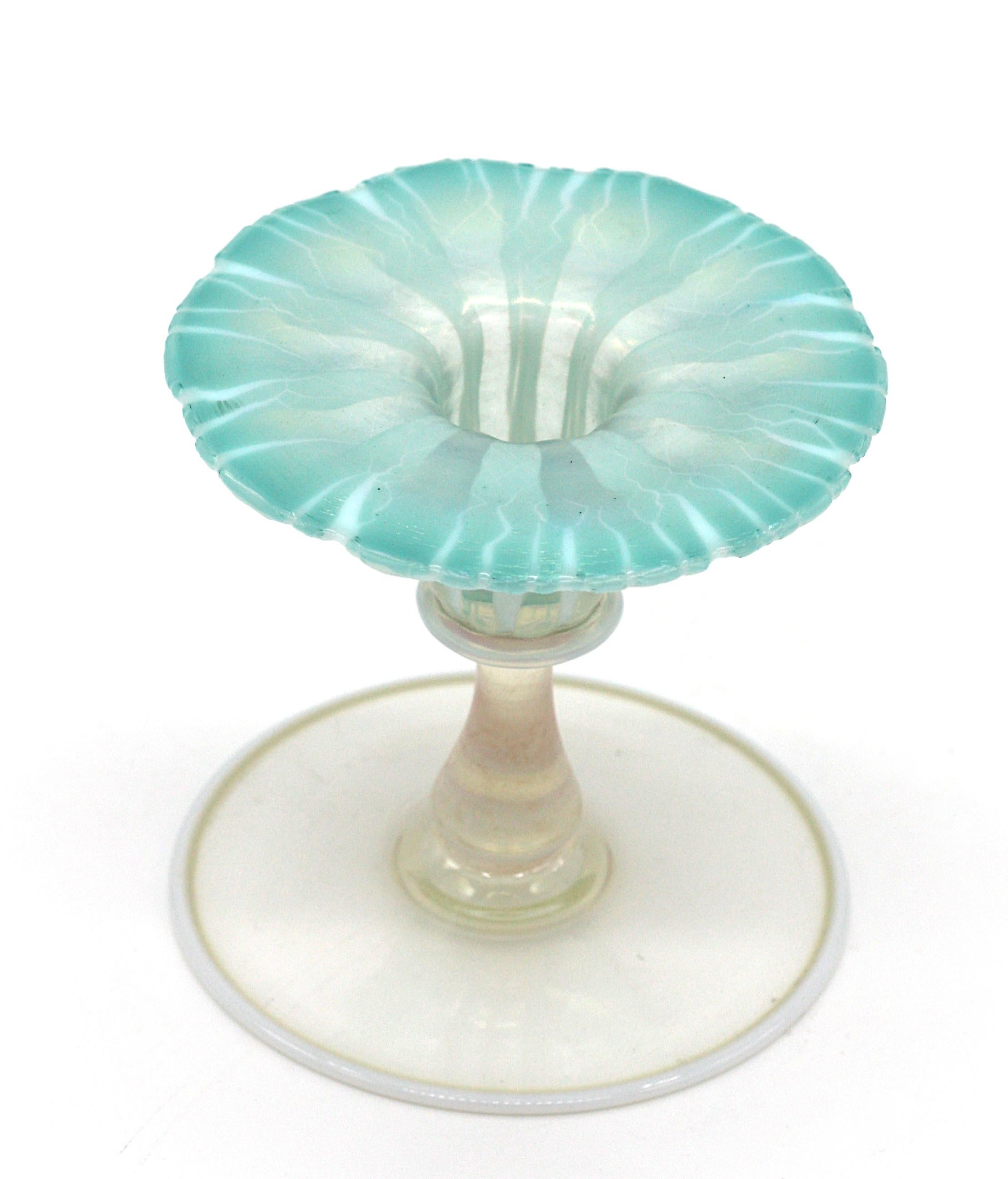 A Tiffany Favrile glass morning glory candlestick.
Circa 1918-28.
In aqua blue, opalescent and colorless glass, signed L.C.T.-Favrile
Measure: height 3.75 in. (9.52 cm.)
Condition report.
Overall good condition and appearance.