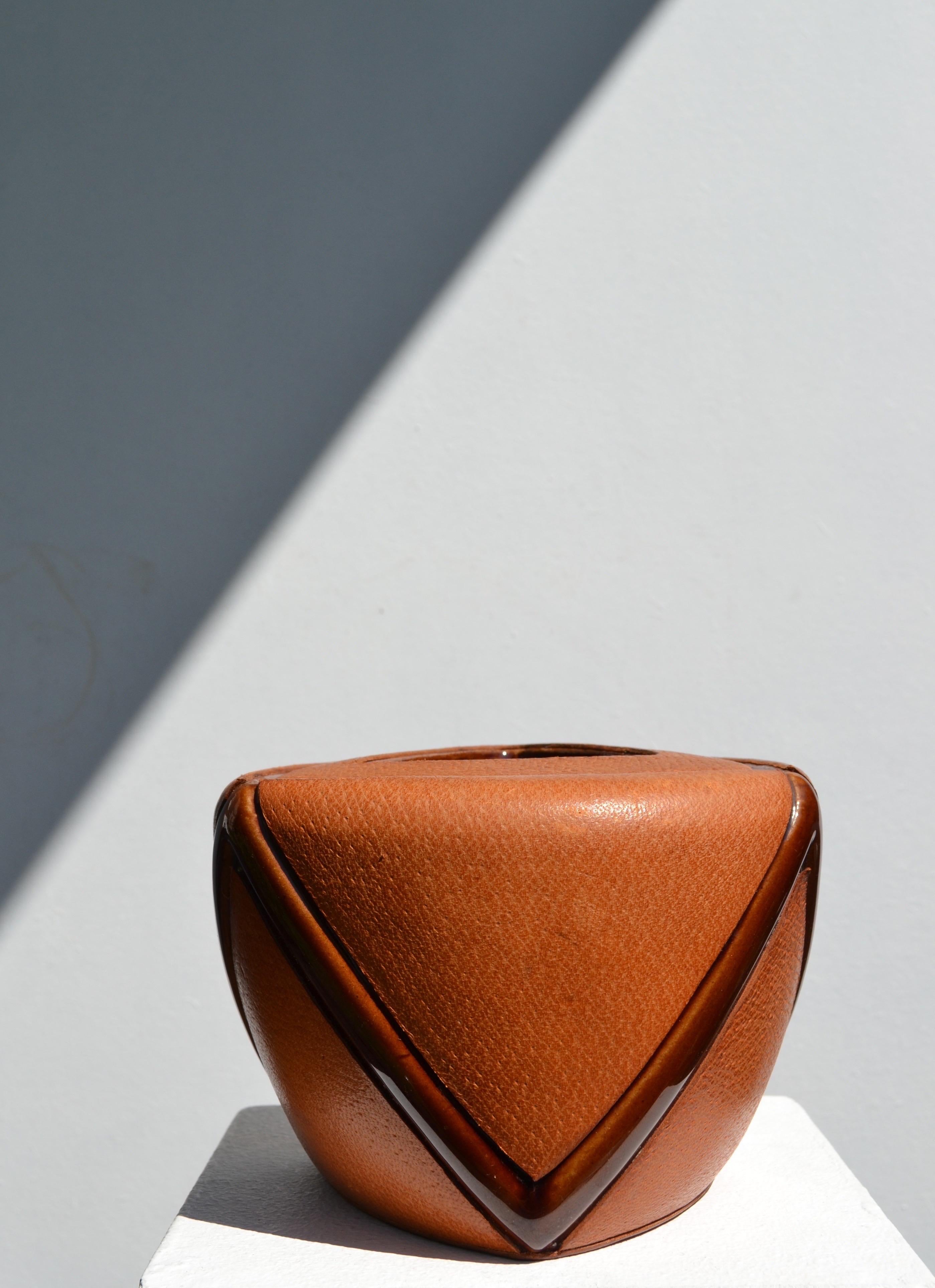 Un raro y refinado tarro para tabaco fabricado en cerámica y totalmente envuelto en cálida piel de color canela, atribuido a la apreciada Maison Longchamp de París. La tapa de cerámica a juego, también forrada en piel, completa el diseño cohesionado