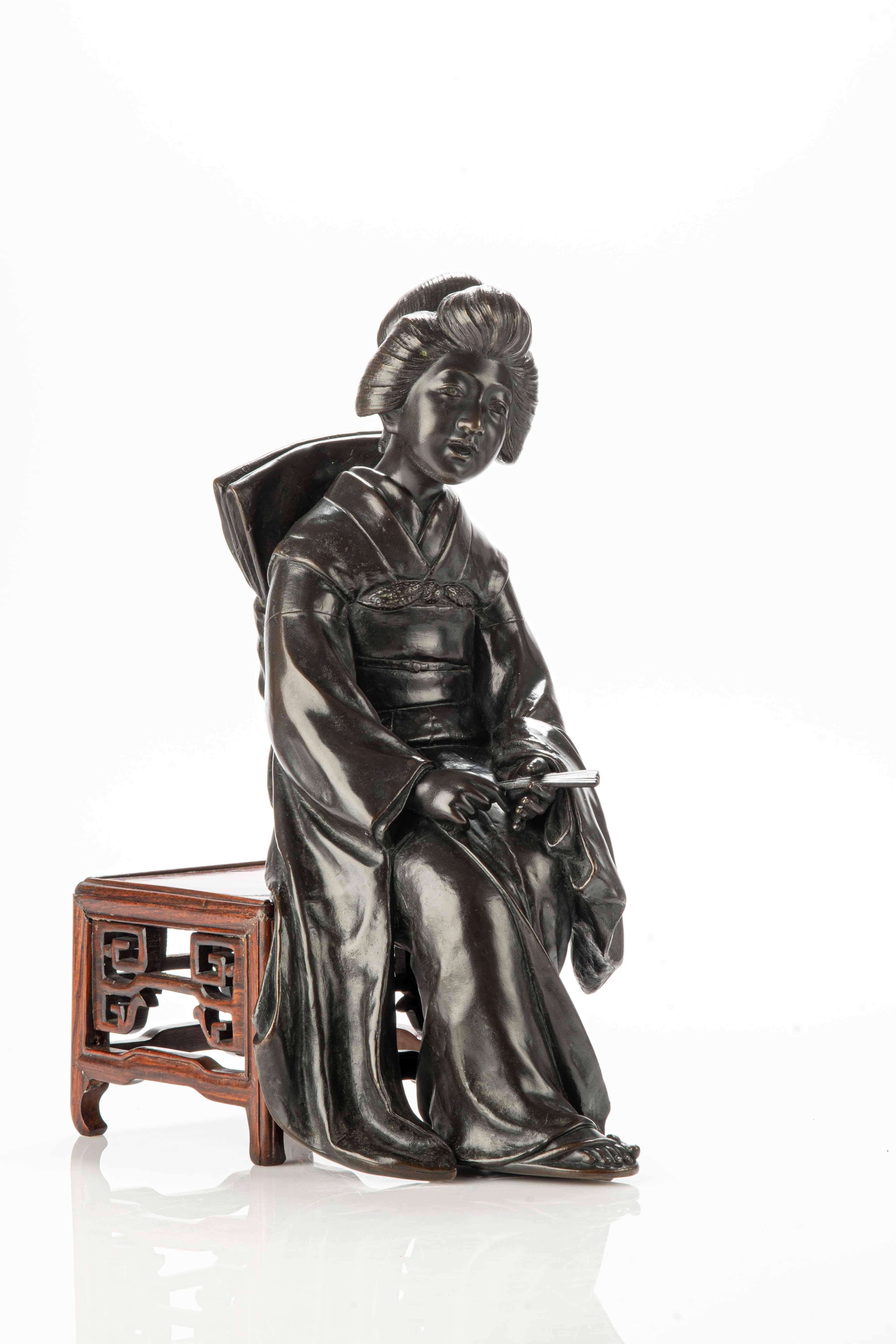Tokyo school bronze sculpture depicting a geisha sitting on a wooden bench. The figure of the geisha is portrayed in a moment of deep reflection, with a fan held in her hands. She wears a luxurious festive kimono, embellished with rich details and a