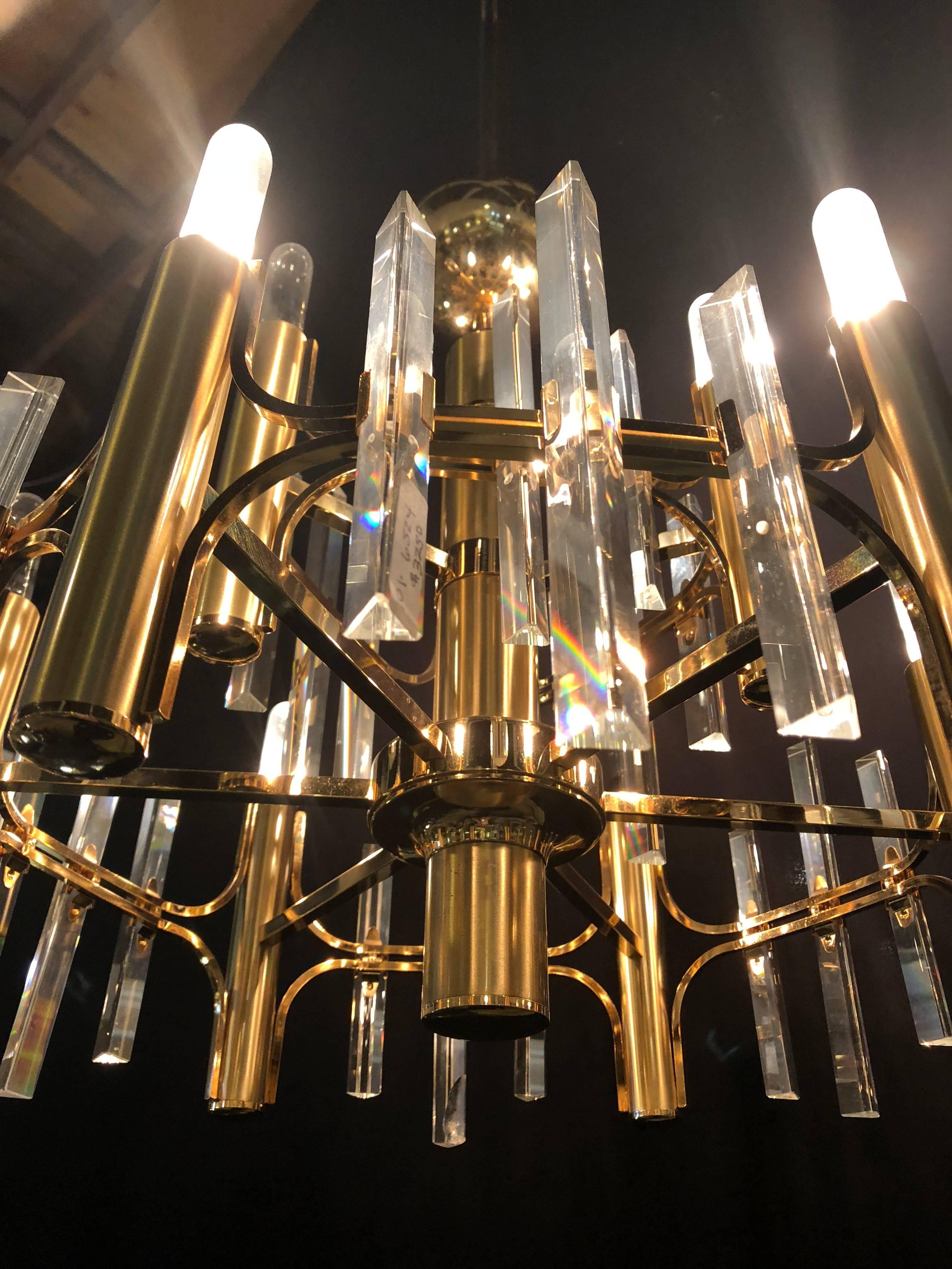 A Tommi Parzinger inspired Hollywood Regency style brass chandelier with crystal prisms. This chandelier has nine brass cylindrical lights spaced by crystal prisms and an adjustable finished pole measuring 17 inches. A fine representation of the Art