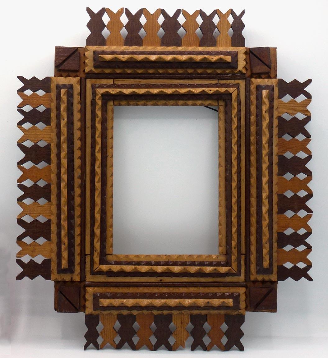 This is a tramp art frame with a very attractive design of light and dark woods, and a pieced openwork border. It has a clear, somewhat glossy lacquer or varnish finish. The condition is excellent, with one very small chip missing on the lower