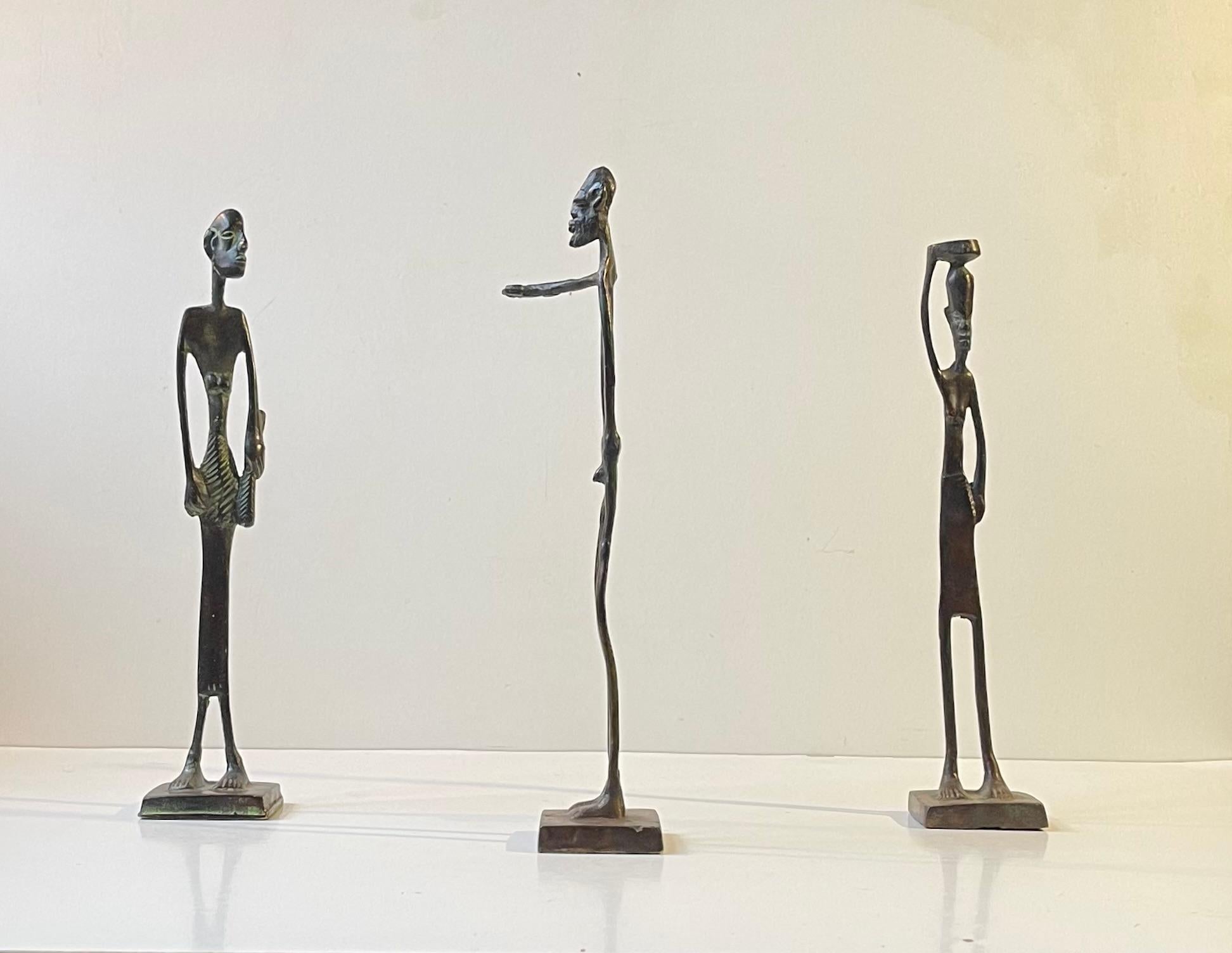 Un trio de sculptures vintage en bronze africain. L'une d'entre elles représente un homme nu/un homme tribal au bras tendu, une autre une femme portant un bol sur la tête et une autre encore une femme en pagne portant un bâton. L'ensemble a été