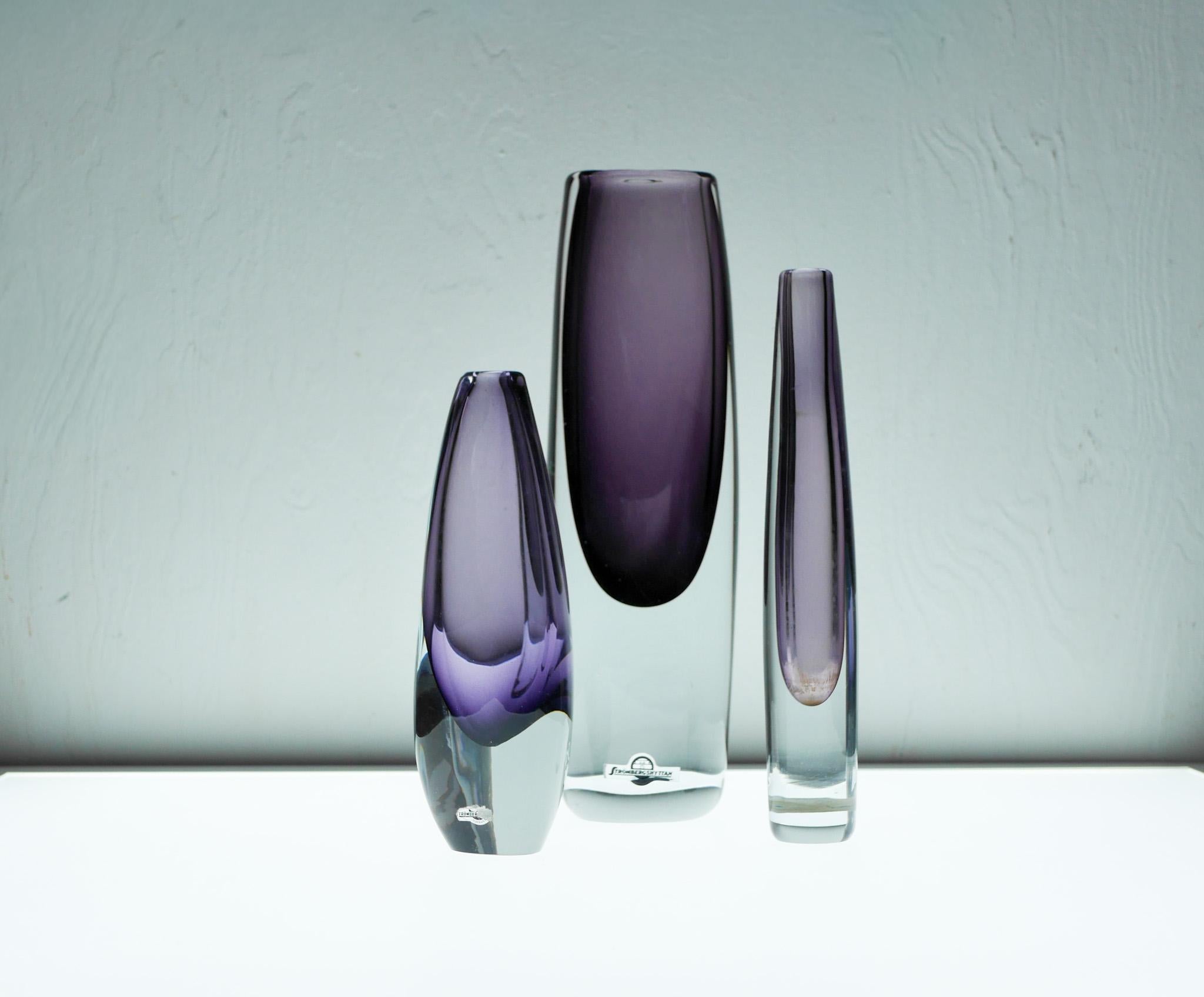 Ein auffälliges Trio schwedischer Sommerso-Kunstglasvasen, mundgeblasen und signiert von den bekannten Designern Gunnar Nylund und Asta Strömberg für Strömbergshyttan. Jedes Stück zeigt einen reichhaltigen, leuchtenden violetten Kern, der von klarem