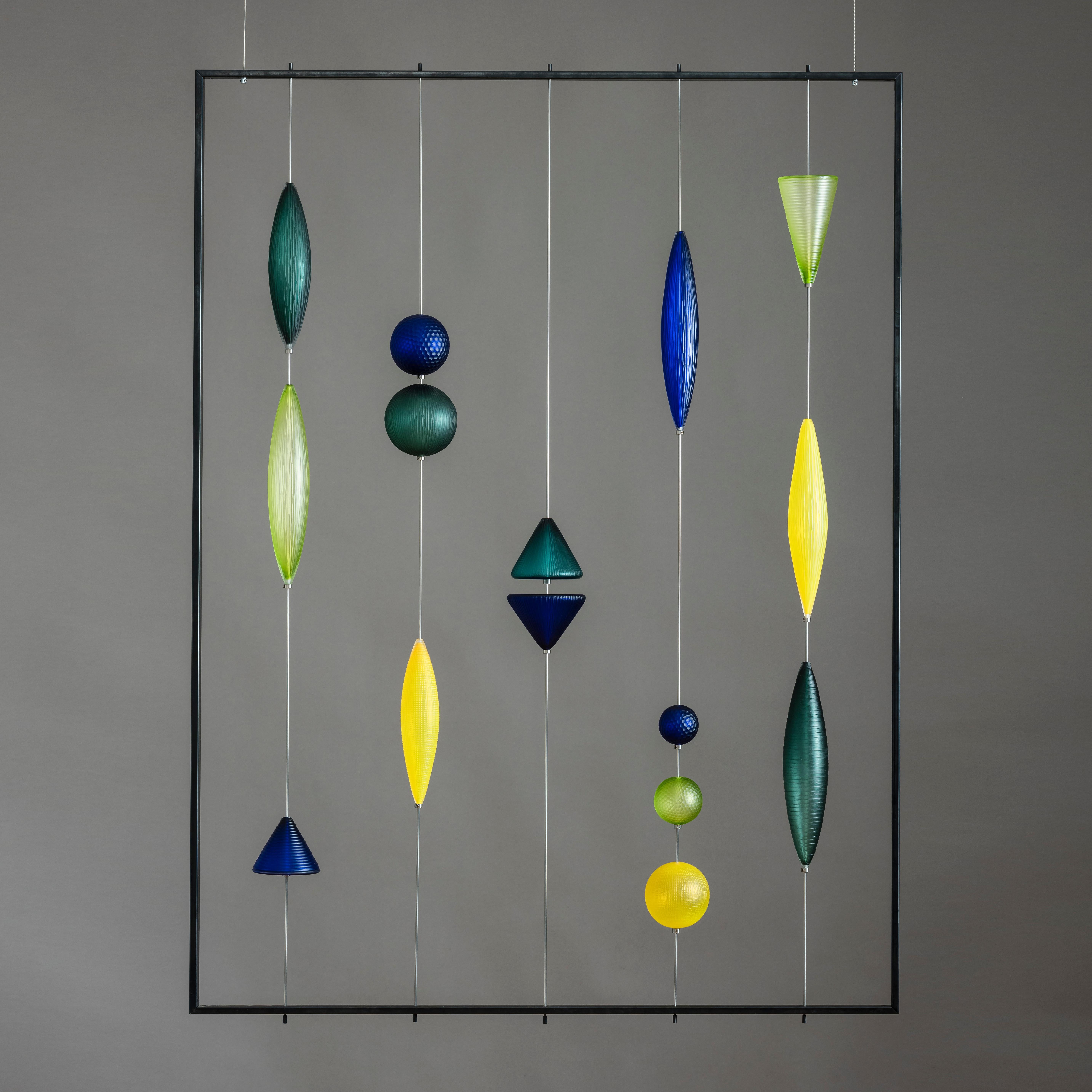 A Tropical Memory is a unique hanging glass with steel frame sculpture in yellow, blue, green and jade by Philip Baldwin & Monica Guggisberg. Scandinavian and Venetian glassmaking techniques come together in their artworks to create beautiful