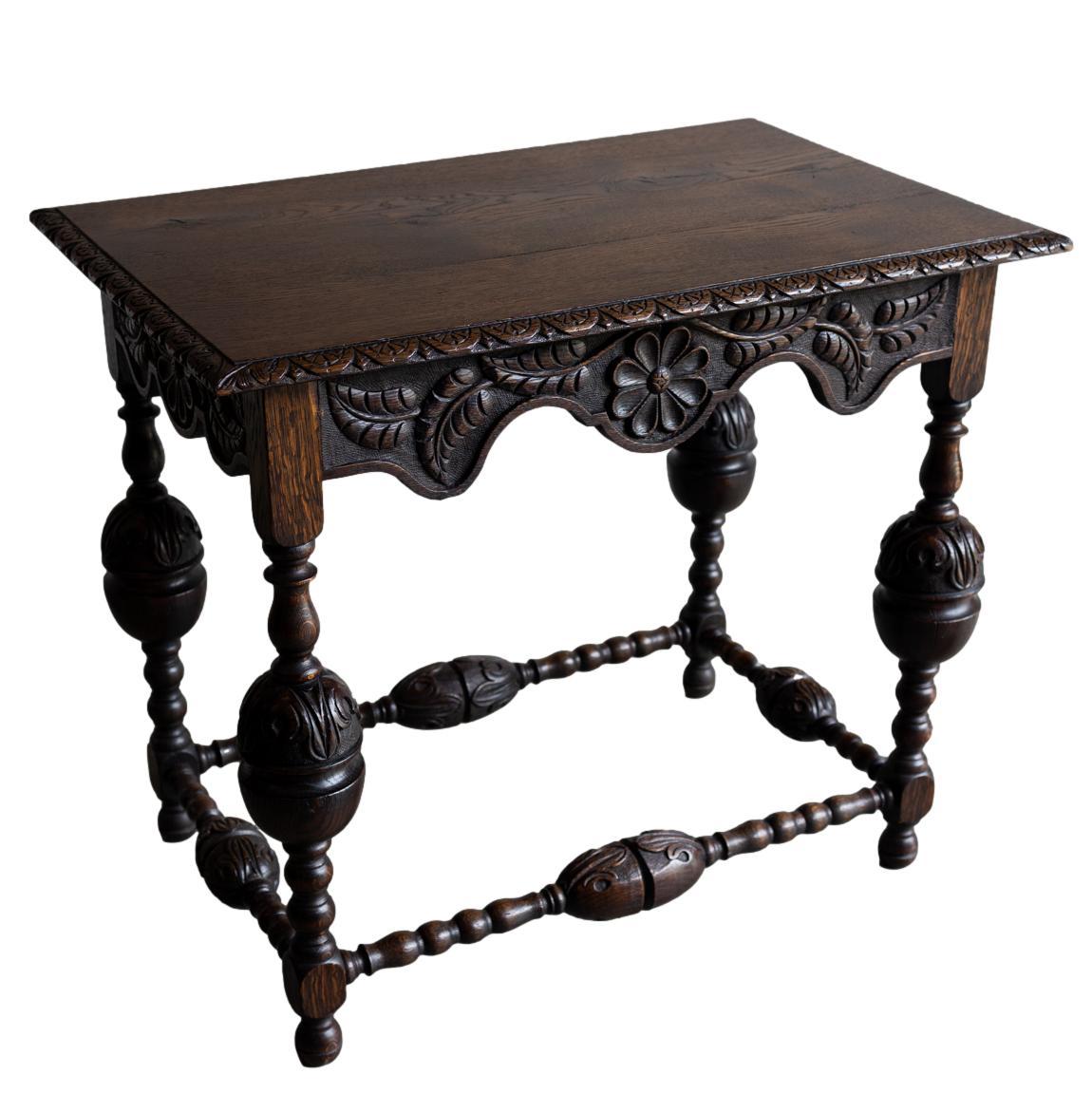 A Tudor-Style Carved Oak Center Table, the rectangular top with a floral fan and dart molded edge, above a shaped apron carved with a daisy medallion and carved leaves to all four sides, with foliate-carved cup-and-cover legs joined by stretchers