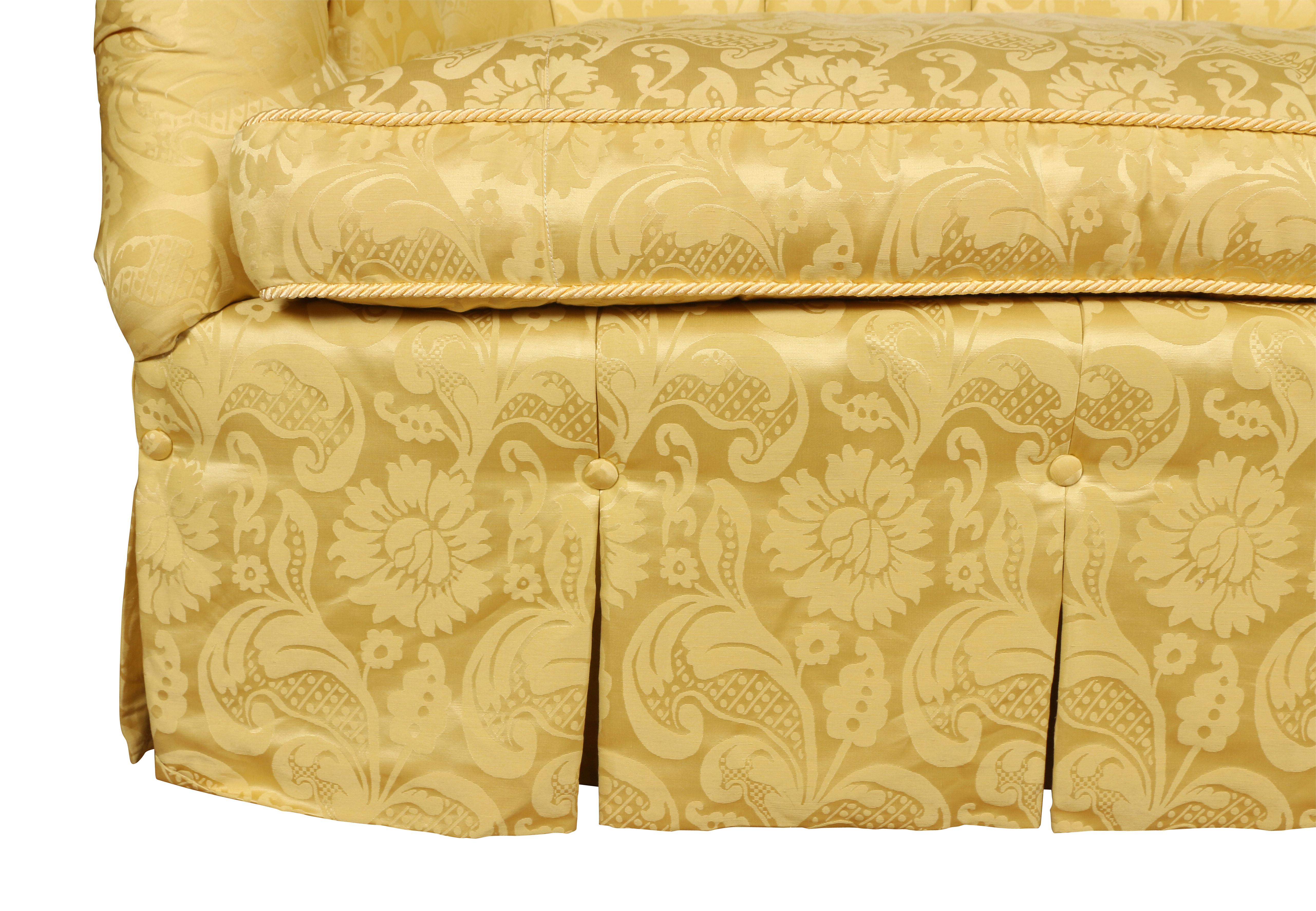 A charming loveseat with a shaped, tight tufted back and rolled arms. A loose seat cushion and a skirted bottom with buttons. The sofa is upholstered in a yellow silk damask with braided trim. One of a pair in our inventory. 