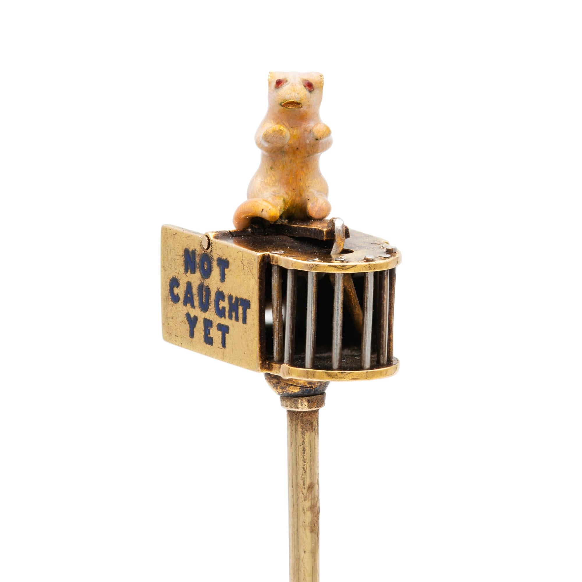 A turn of the 20th century mouse and trap stick-pin, the fine enamelled mouse sitting on the top of a trap with blue enamel inscription “not caught yet”, all made in yellow gold, with gold pin, circa 1900, the jewelled part measuring 1.5x1.9cm gross