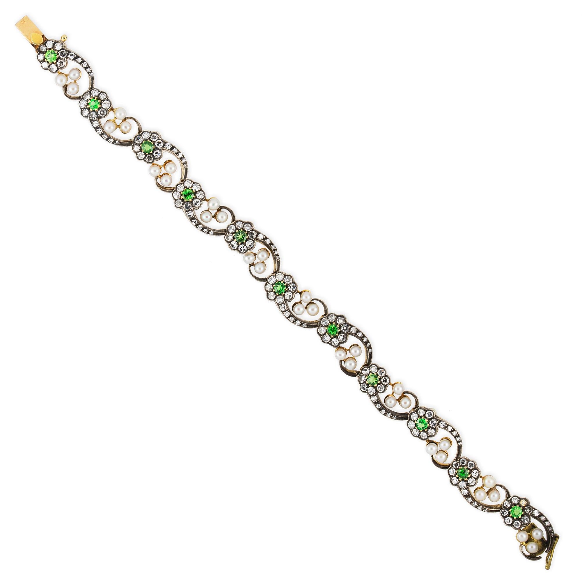 A turn of the century demantoid garnet and diamond bracelet, consisted of eleven links each bearing a flower with a demantoid garnet centre, swiss-cut diamond encrusted petals and stems terminating to pearl-set trefoil, mounted in silver and yellow