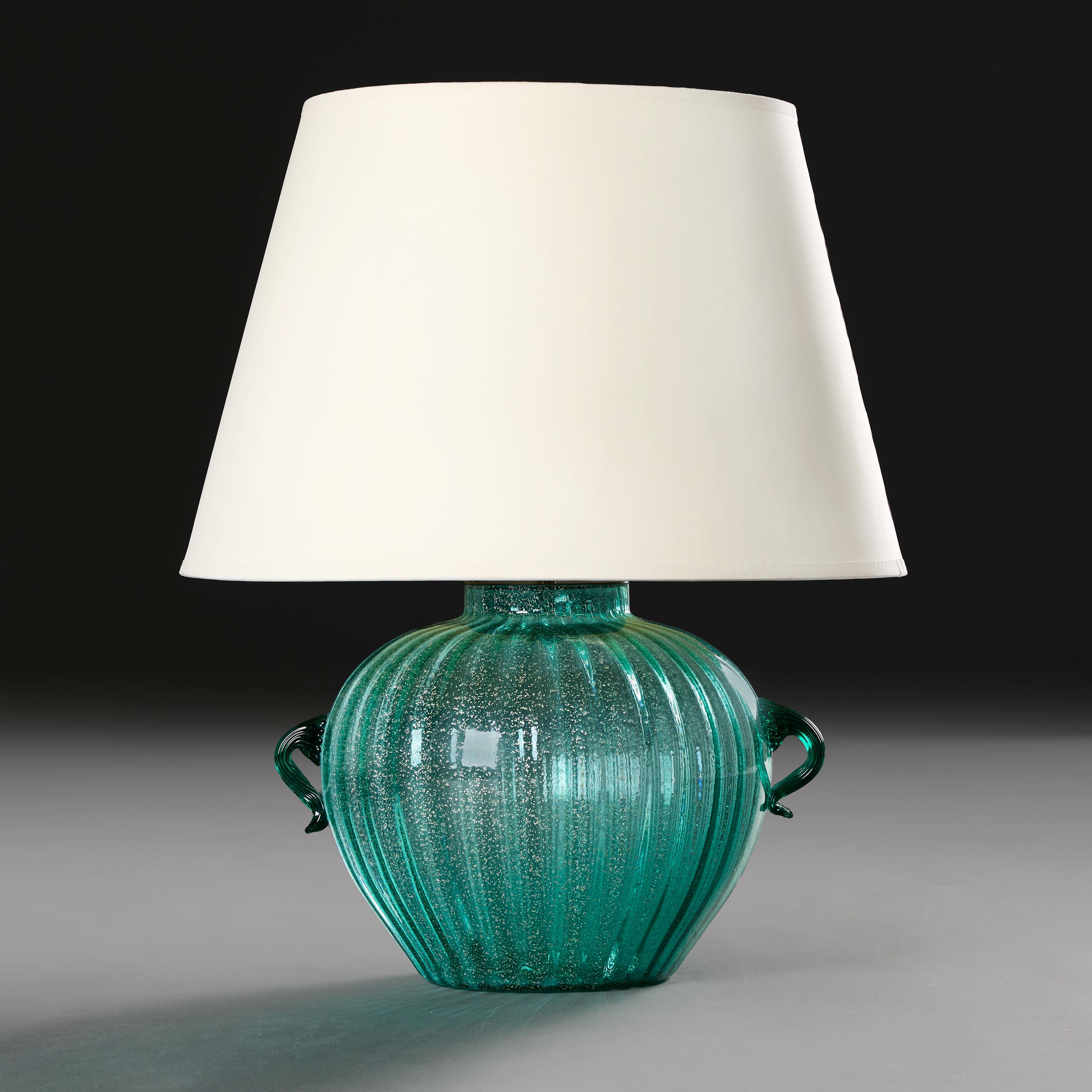 Italy, circa 1940

A twentieth century Murano vase of swollen form, in turquoise glass with silver aventurine flecks throughout and hot-applied serrated handles, now mounted as a lamp.

Height of vase: 24.00 centimetres.

Height with shade: 53.00