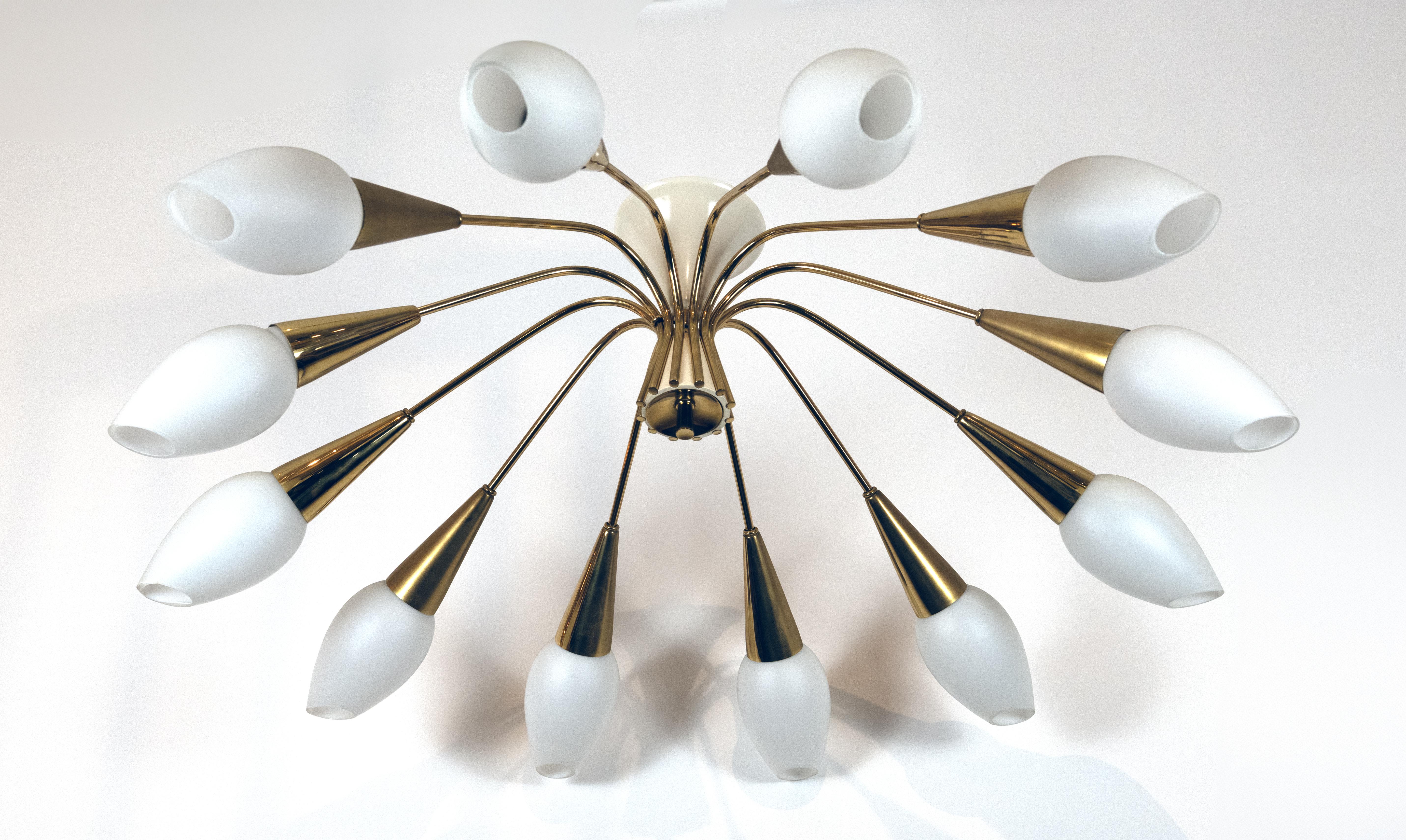 A twelve-light mid-century ceiling mounted fixture. The ivory lacquered frame and canopy issuing twelve brass arms issuing tulip-shaped frosted glass shades fitted with articulated brass cups. In the style of Carlo Mollino, circa 1960. Price