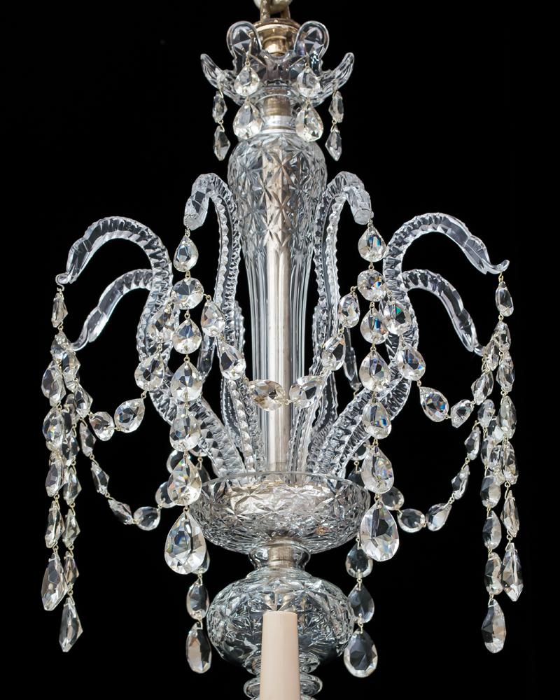 A pressed and cut glass chandelier in Georgian style with multi baluster shaft issuing drop hung serpentine corona the receiver plates supporting twelve notch cut arms terminating with pressed van-dyke drip pans and candle nozzles the chandelier