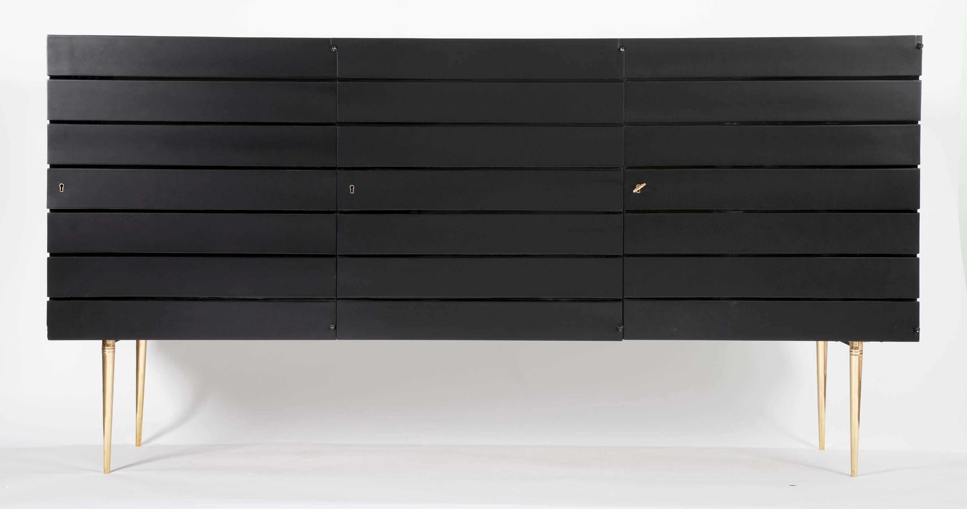 A flat black sideboard with high gloss recessed lines. Italian circa 1965. Case has three doors two housing shelves on either side of 5 drawers.
  