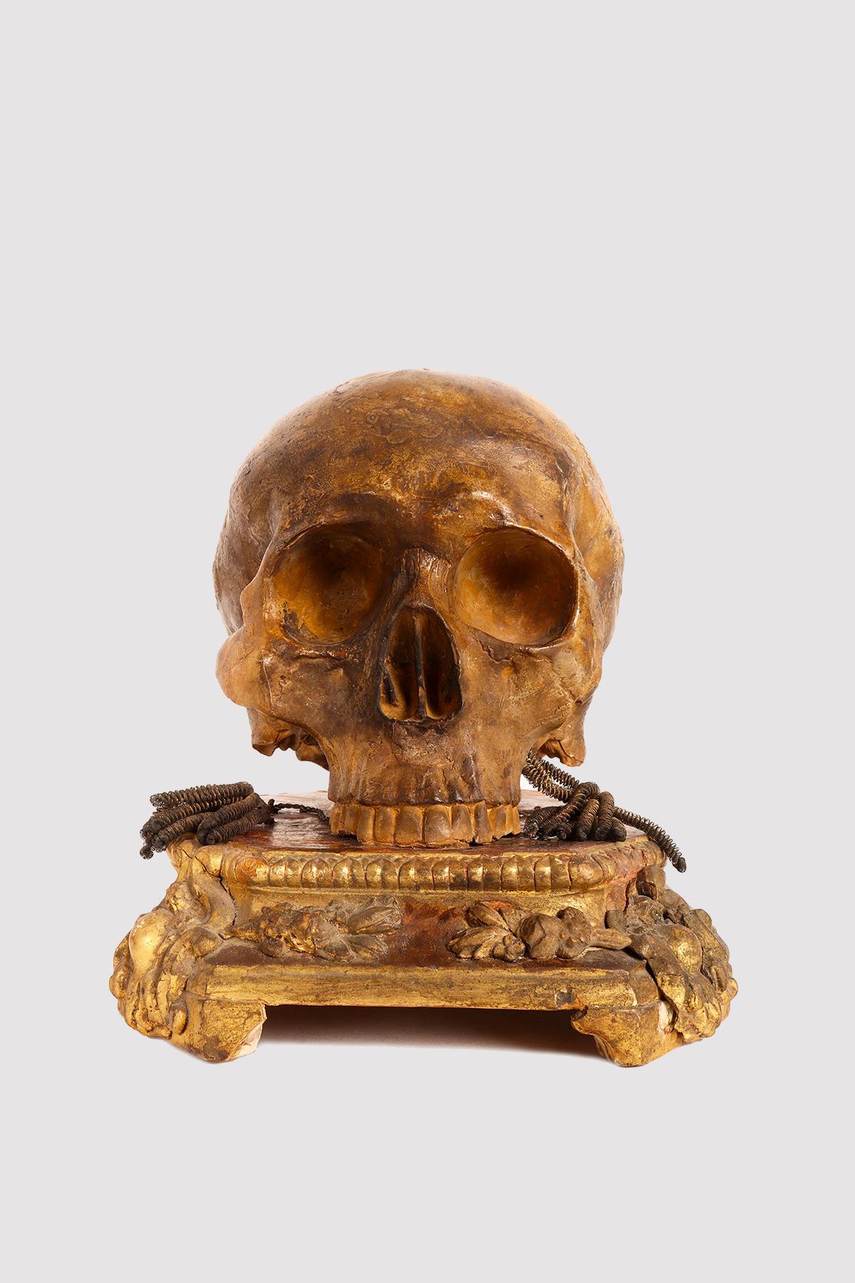 Au-dessus de la base en bois doré se trouve une Vanitas, une sculpture en plâtre peint représentant un crâne humain. Italie, début du 19e siècle.