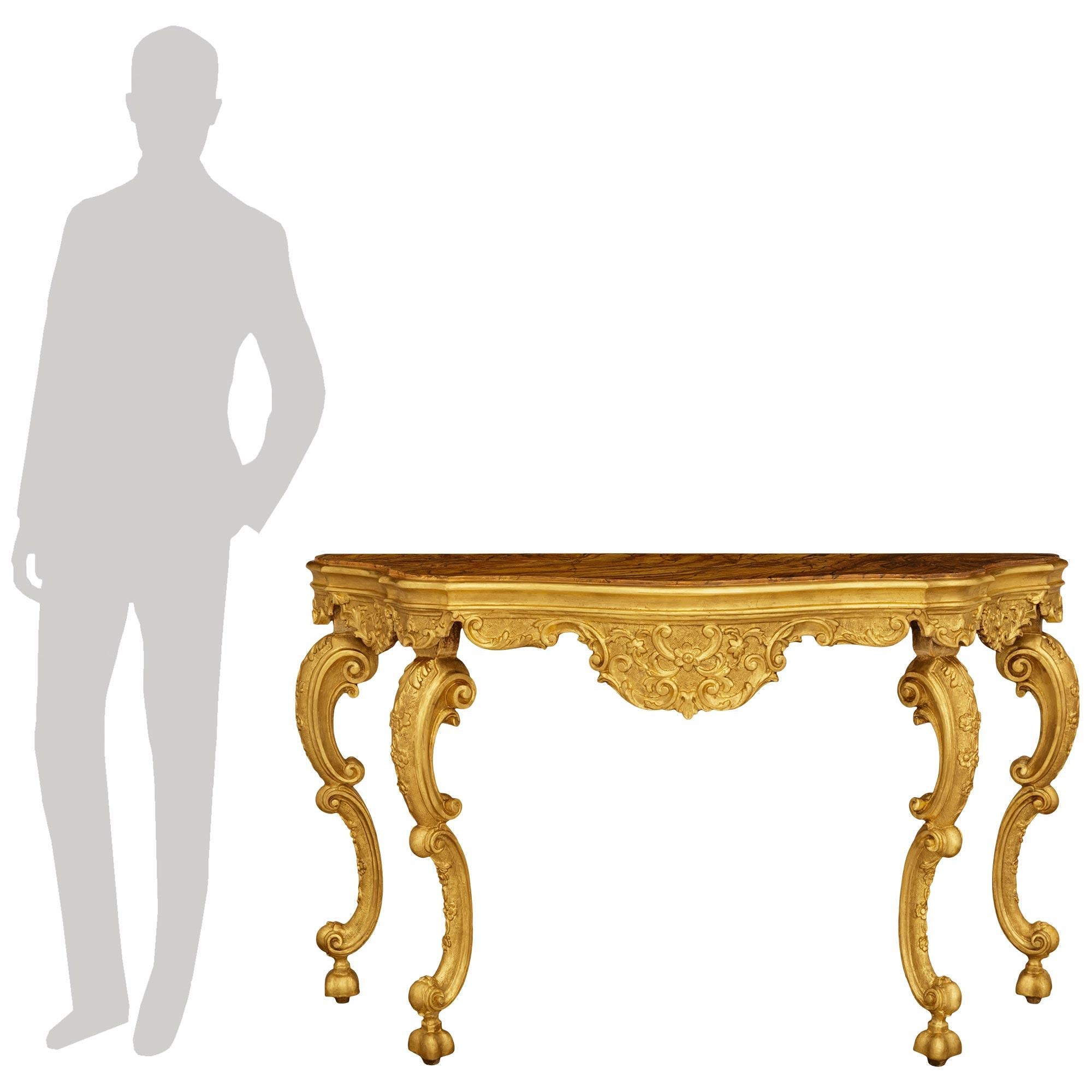A stately and most elegant Venetian 18th century Giltwood and faux painted marble console. This unique freestanding console is raised on wonderful bell shaped feet below the double scrolled legs accented with foliate carvings. The legs lead up to