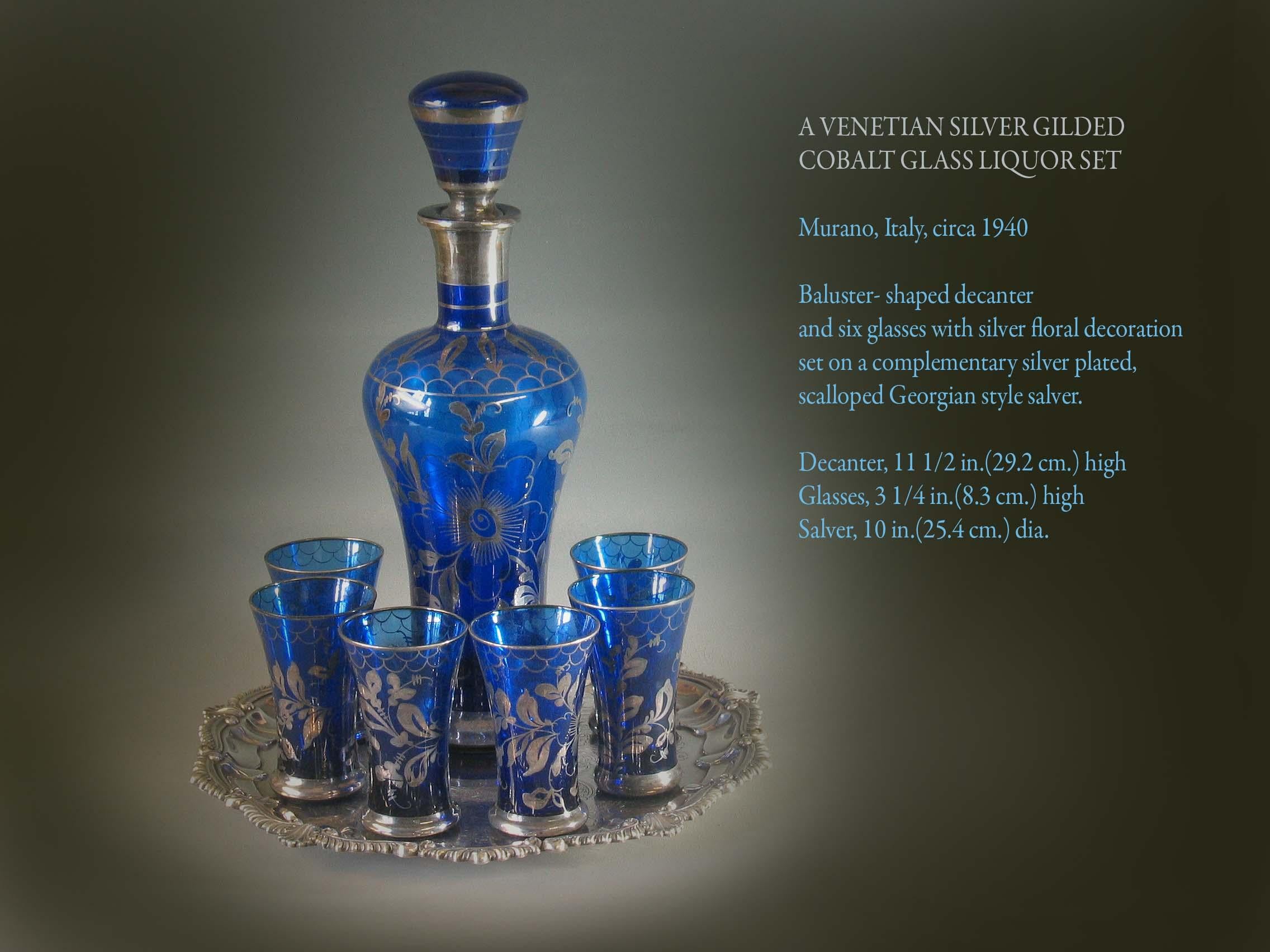 A Venetian silver gilded cobalt glass liquor set

Murano, Italy, circa 1940.

Baluster- shaped decanter
and six glasses with silver floral decoration
set on a complementary silver plated, 
scalloped Georgian style salver.

Measures: