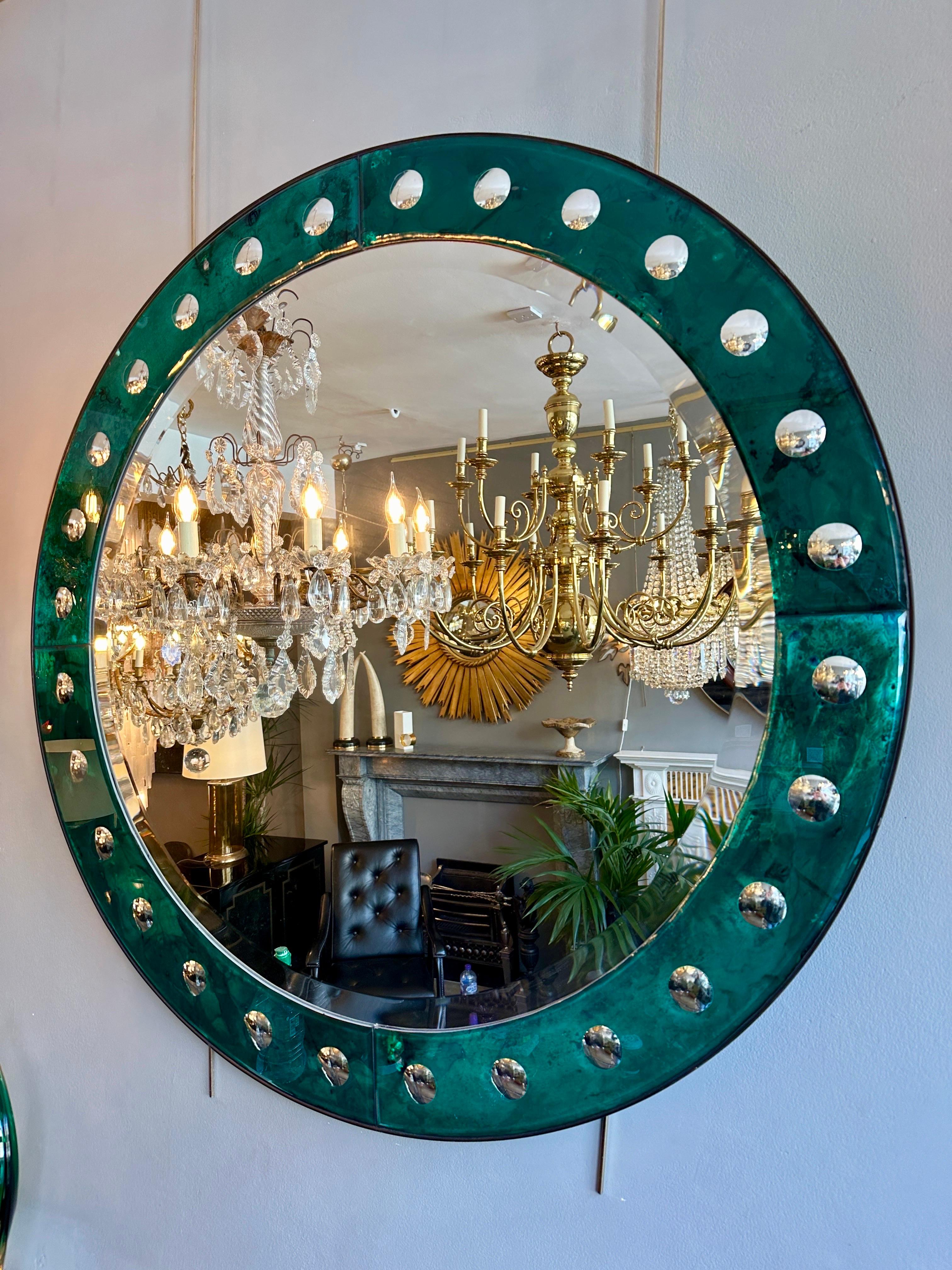 A large circular bevelled mirror with distressed green bordered frame decorated with reverse cut mirrored spheres. Black steel banded outer edge. 