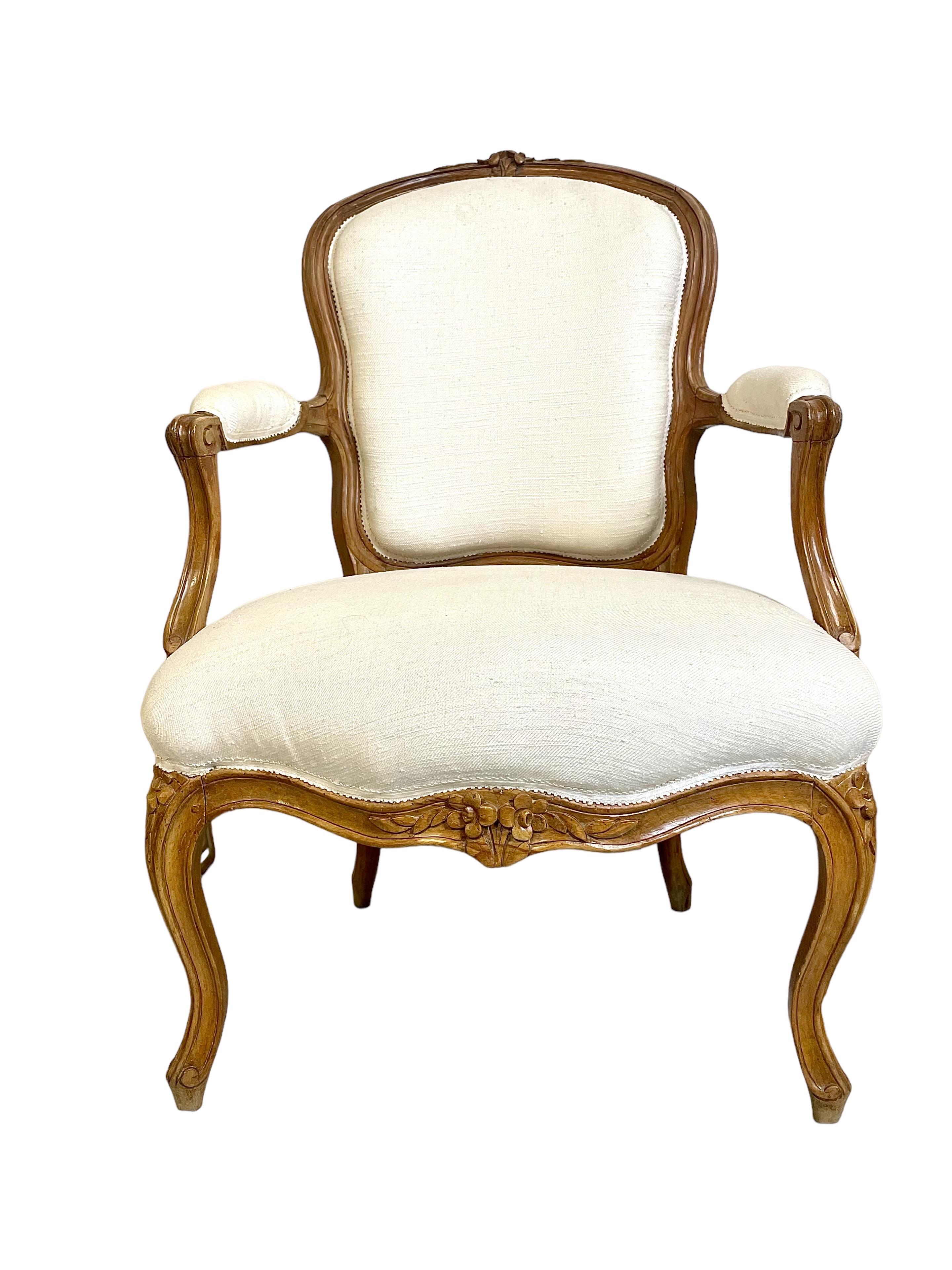 Très chic paire de fauteuils cabriolets d'époque Louis XV, en bois naturel, leurs armatures sculptées avec beaucoup de finesse et garnies de tissu crème. De délicieux motifs floraux sculptés à la main ornent la couronne du dossier, le tablier et le