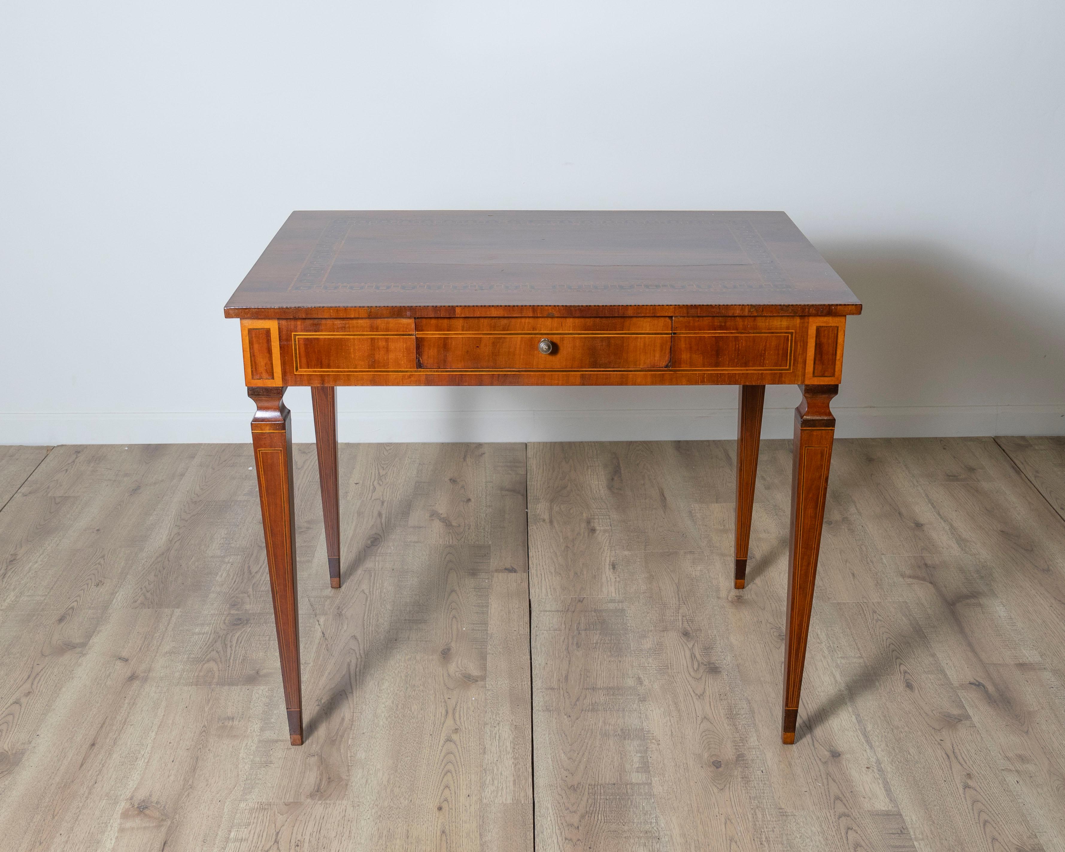 This refined Italian walnut writing table or desk is a beautiful example of neoclassical craftsmanship, combining graceful form with intricate detailing. The rectangular top is framed by delicate geometric inlays, showcasing expert marquetry work