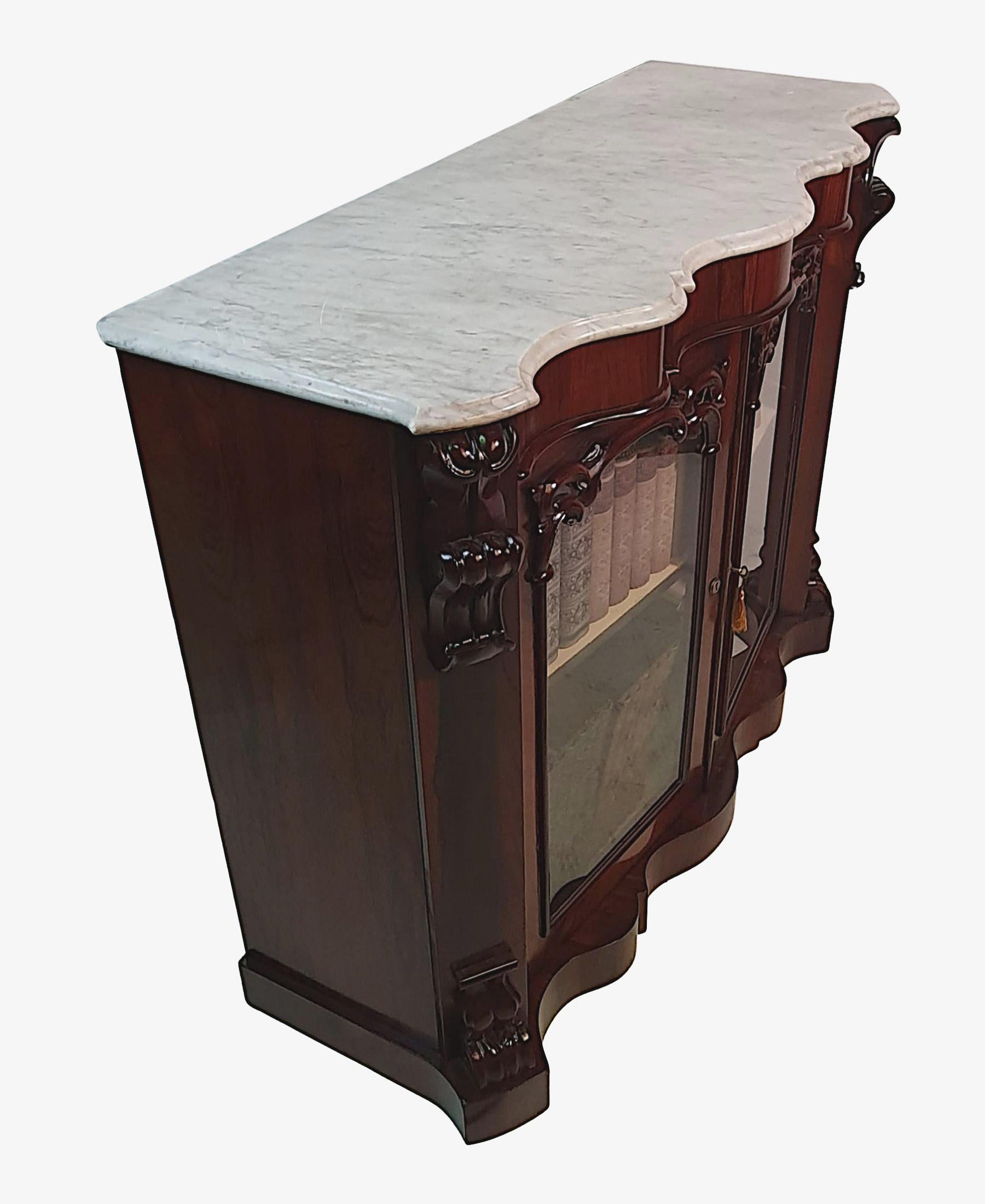 A very fine 19th Century fruitwood side cabinet or bookcase. The Carrara White marble top of serpentine form above simple, moulded frieze raised over two reeded and panelled glazed doors surmounted with scrolling leaf motif, flanked with canted