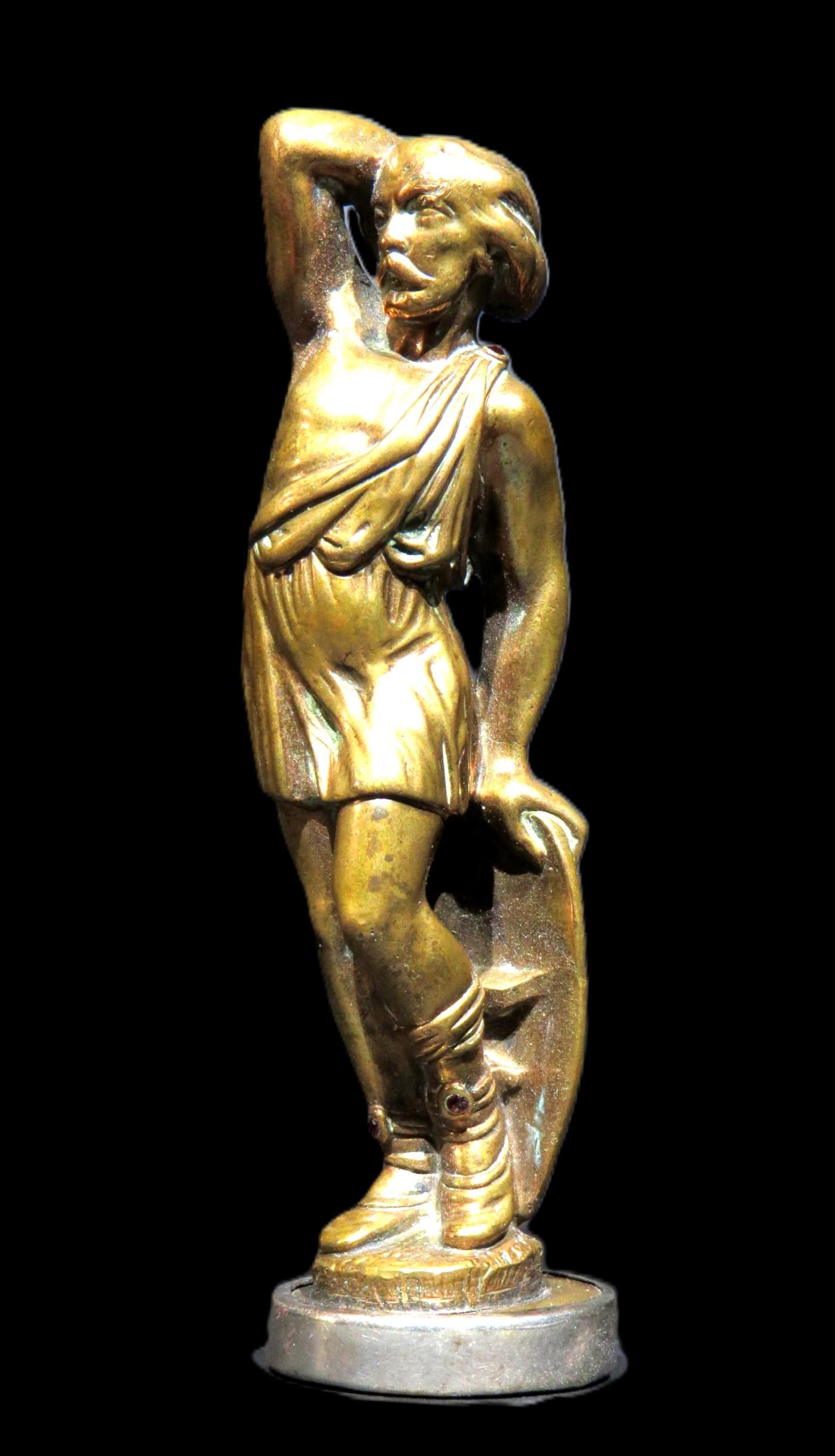 La figura di un guerriero in abiti classici romani, in posizione contrapposta con una mano appoggiata su uno scudo e l'altra che stringe una clava infilata sopra e dietro la spalla. Montato su un monticello roccioso con motivi naturalistici, in cima