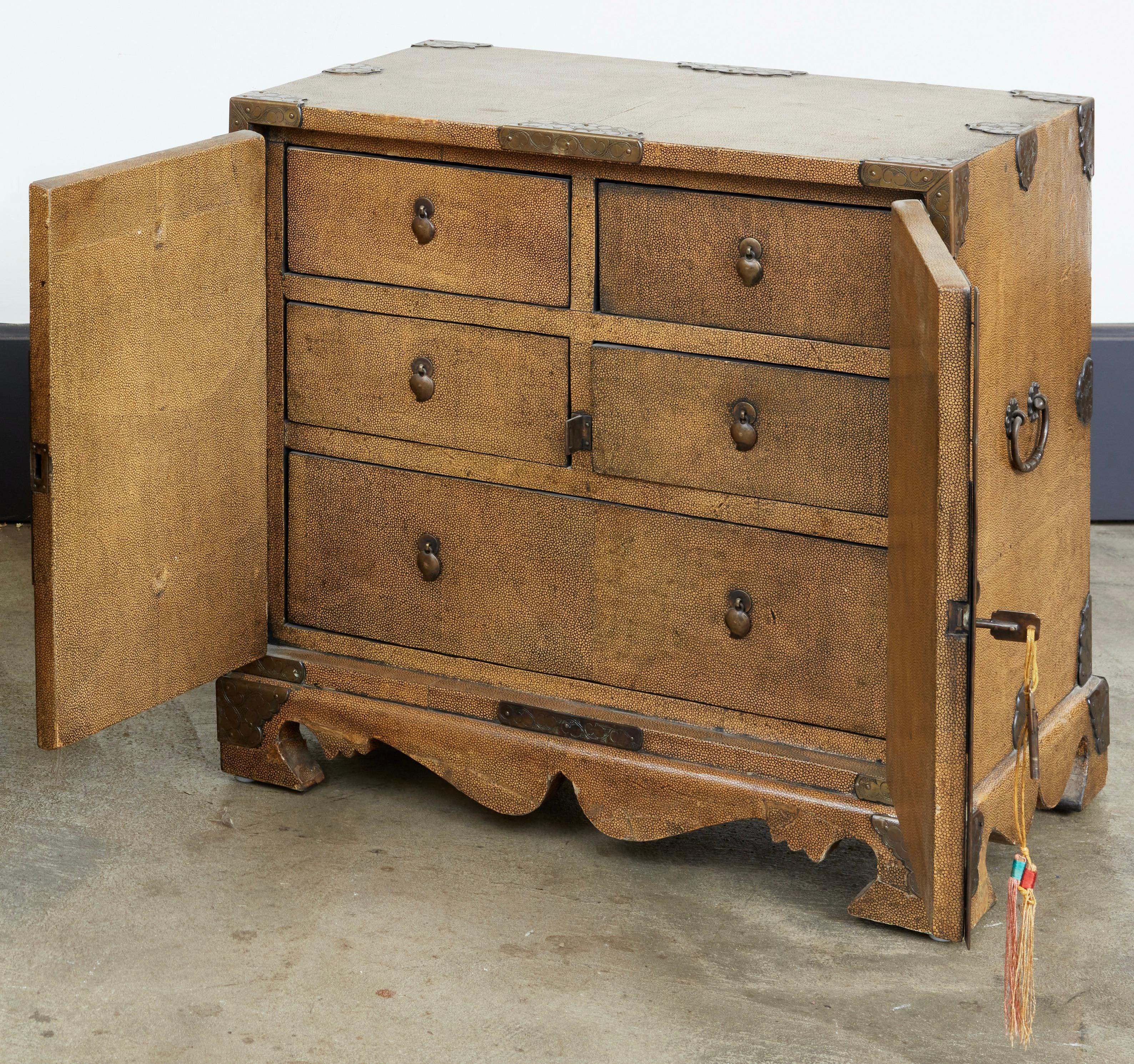 All over finished with shagreen and clad in hammered brass. The 2 doors opening to reveal a fitted interior with 5 drawers.