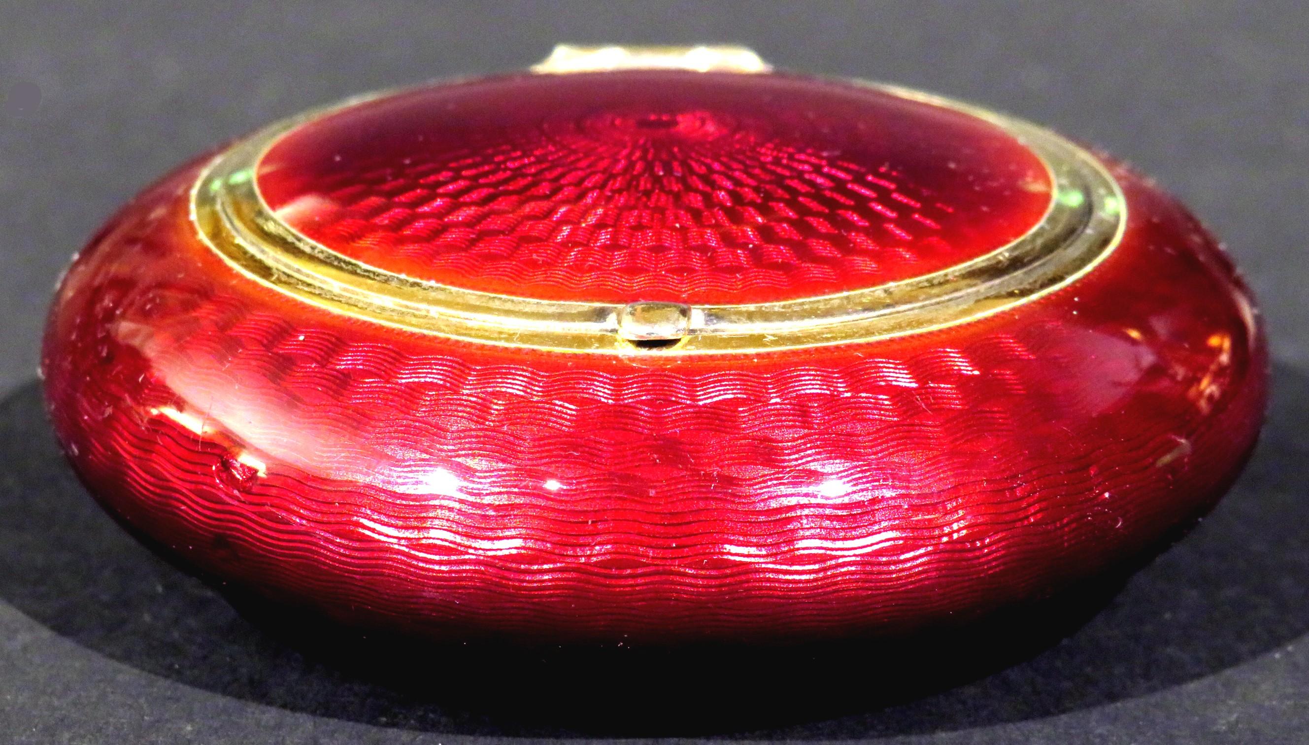 The disc-shaped case decorated in a stunning deep crimson guilloché enamel with a silver trimmed rim. The hinged lid showing a gilded interior surface bearing impressed makers marks for Norwegian artist Marius Hammer & silver purity marks denoting