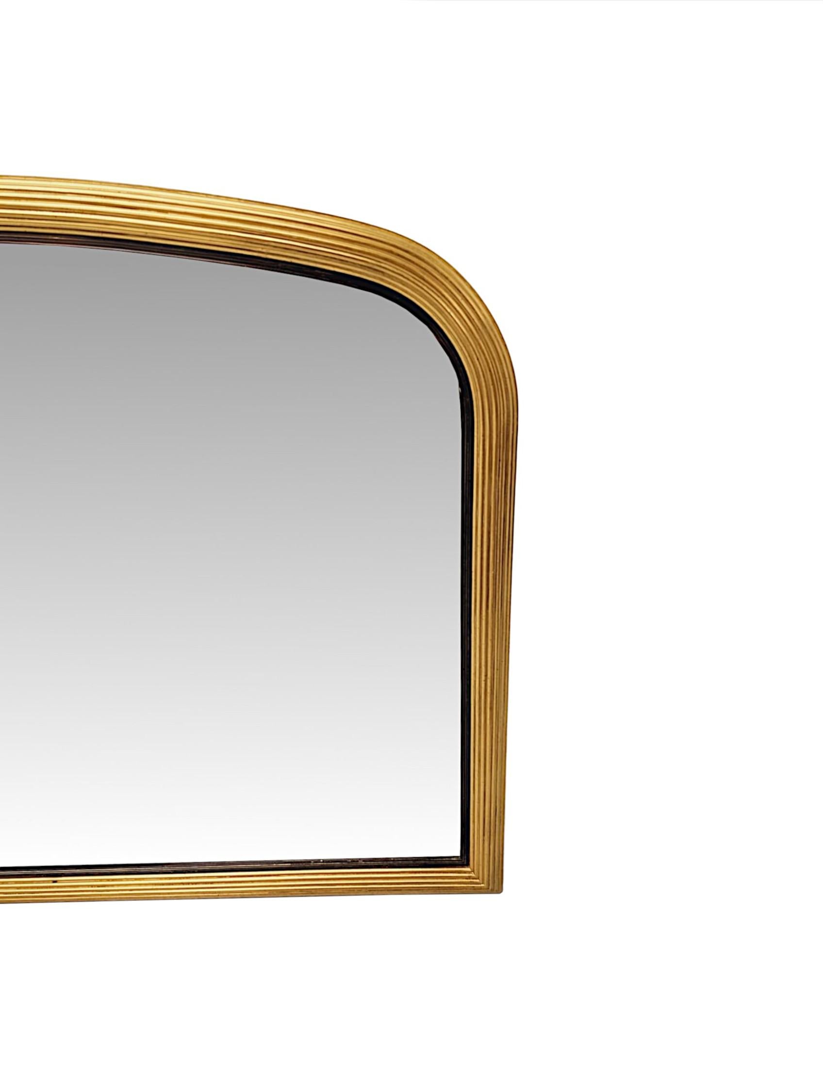 A very fine and unusual Edwardian elegantly simple, giltwood overmantel mirror of exceptional quality and low and wide proportions.  The bevelled and shaped mirror glass plate of archtop form is set within a stunningly carved, moulded and reeded