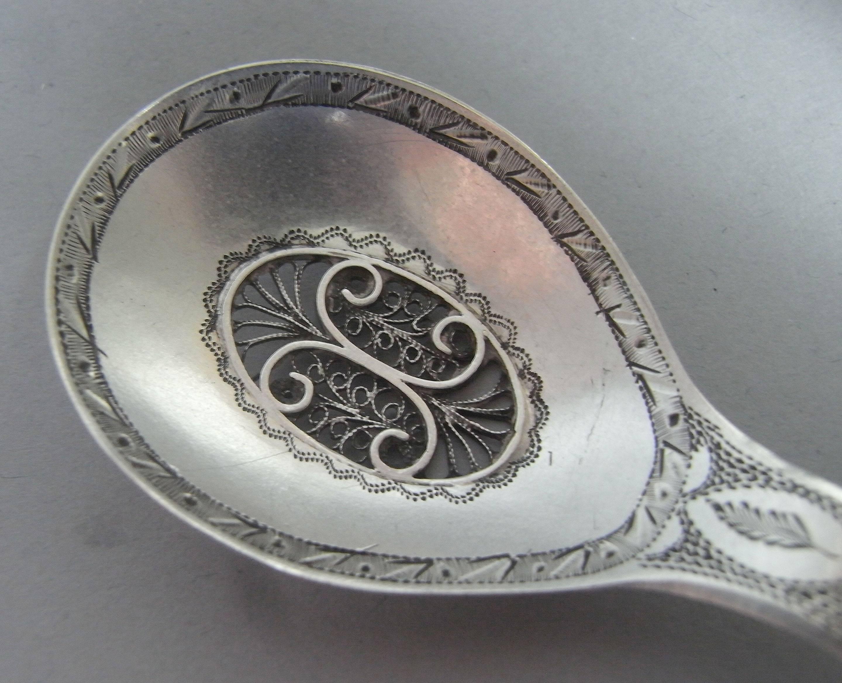The caddy spoon has an oval bowl with prick dot engraved border. The centre is inset with a filigree scroll panel and the handle is engraved with foliate and prick dot designs, in addition to an oval cartouche engraved with a contemporary script