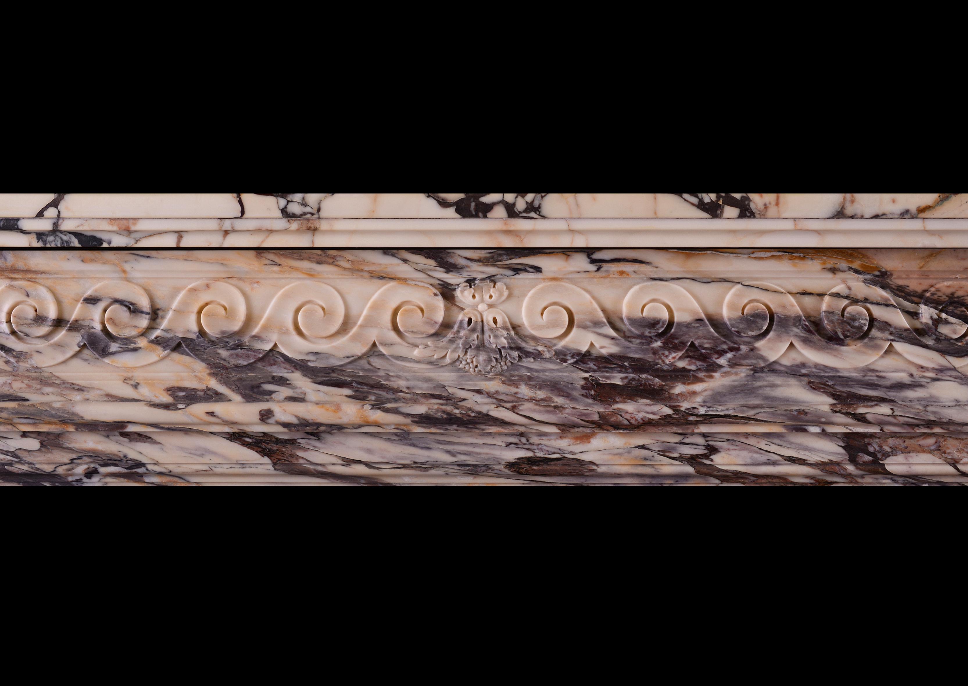 Très belle cheminée Louis XVI en marbre Brèche Violette. La frise sculptée est ornée de rinceaux en forme de c, avec une campanule sculptée au centre. Les jambages à cannelures incrustées de coques sculptées sont surmontés d'une console à volutes et