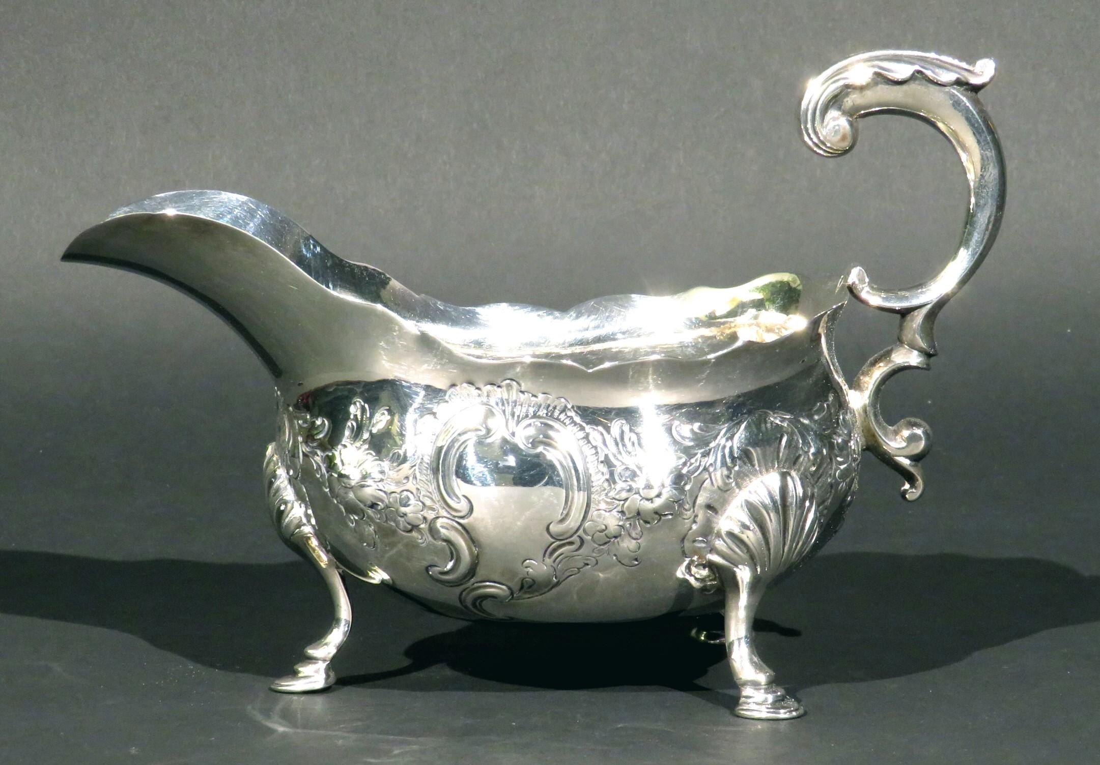 A very fine & generously proportioned mid 18th century Georgian sterling silver gravy boat, showing foliate embossed motifs and a blank cartouche, affixed with an impressive double-scrolled foliate cast handle. Raised overall on cabriole supports