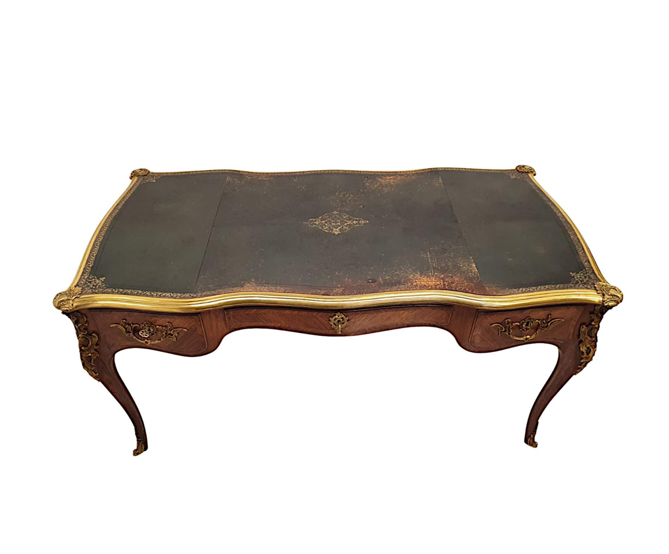 Un raffinato scrittoio della metà del XX secolo in legno di frutto, favolosamente intagliato, ornato di ormolu, con fasce incrociate e intarsiato.  Il piano sagomato e serpeggiante di forma rettangolare con bordo scanalato montato in ormolu con