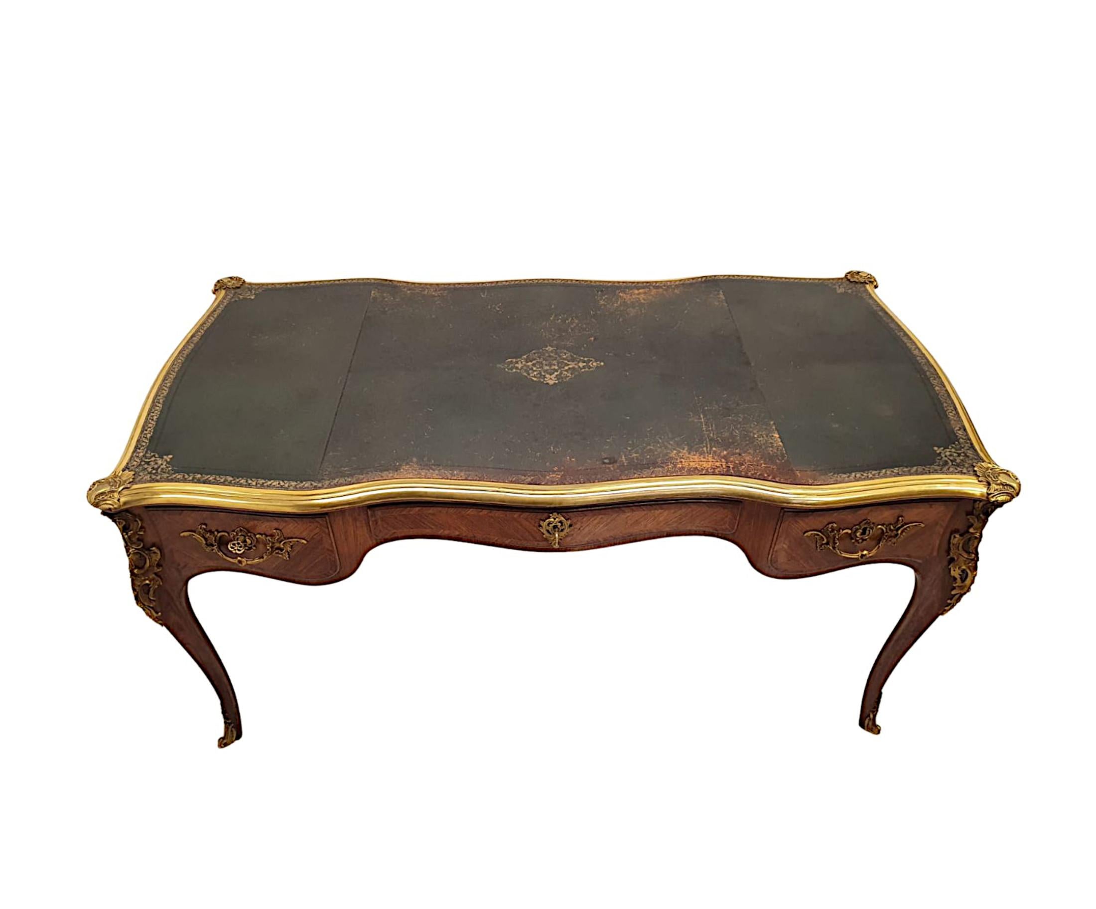 A very fine Mid-20th Century fruitwood bureau plat, fabulously carved, ormolu mounted, cross banded and inlaid throughout. The moulded, serpentine top of rectangular form with fluted ormolu mounted border with intricate scroll, ruffle and foliate