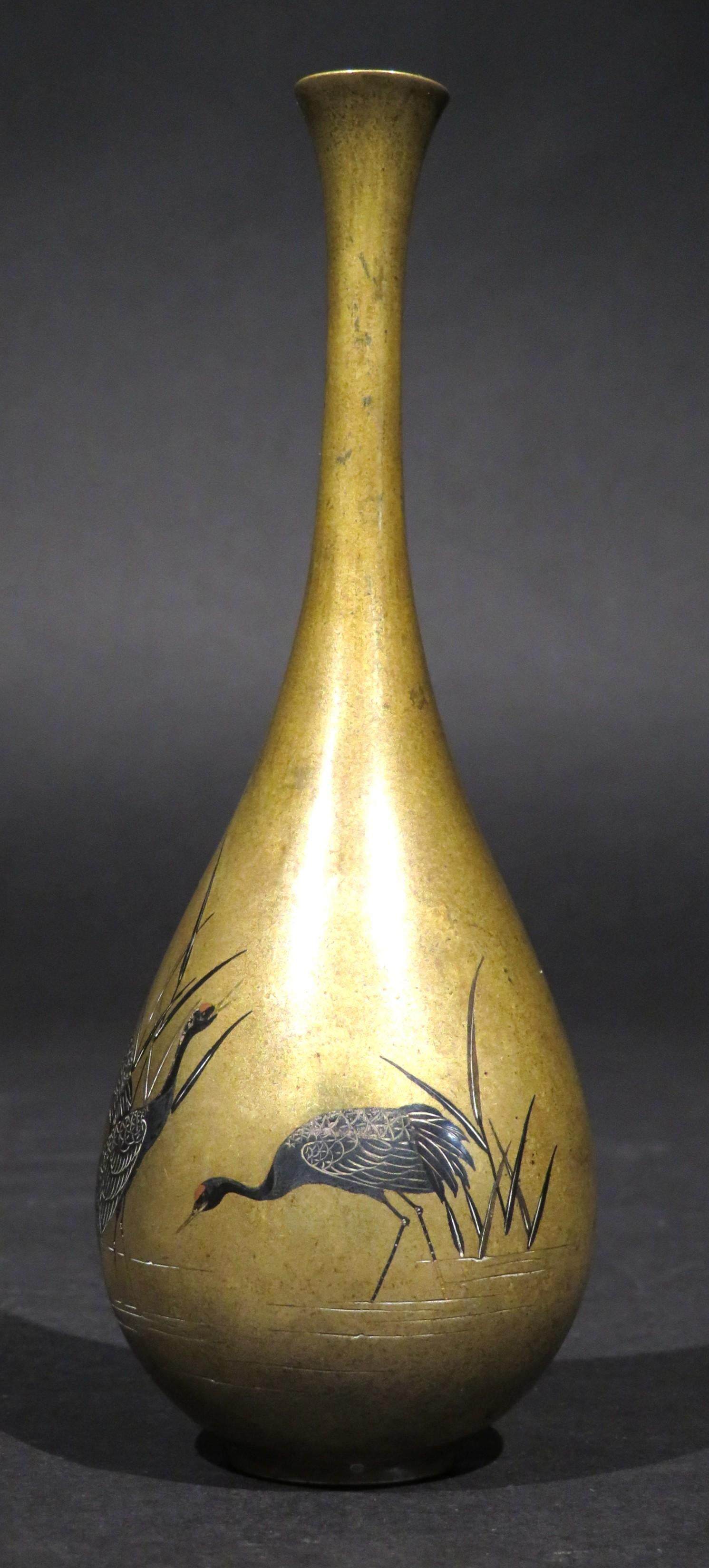 The finely proportioned ovoid shaped body rising to an elongated slender neck with a flaring rim, decorated with motifs of waterfowl standing in a grassy marsh with silvered bodies, accented with copper highlights & gold limbs using both shibuichi &
