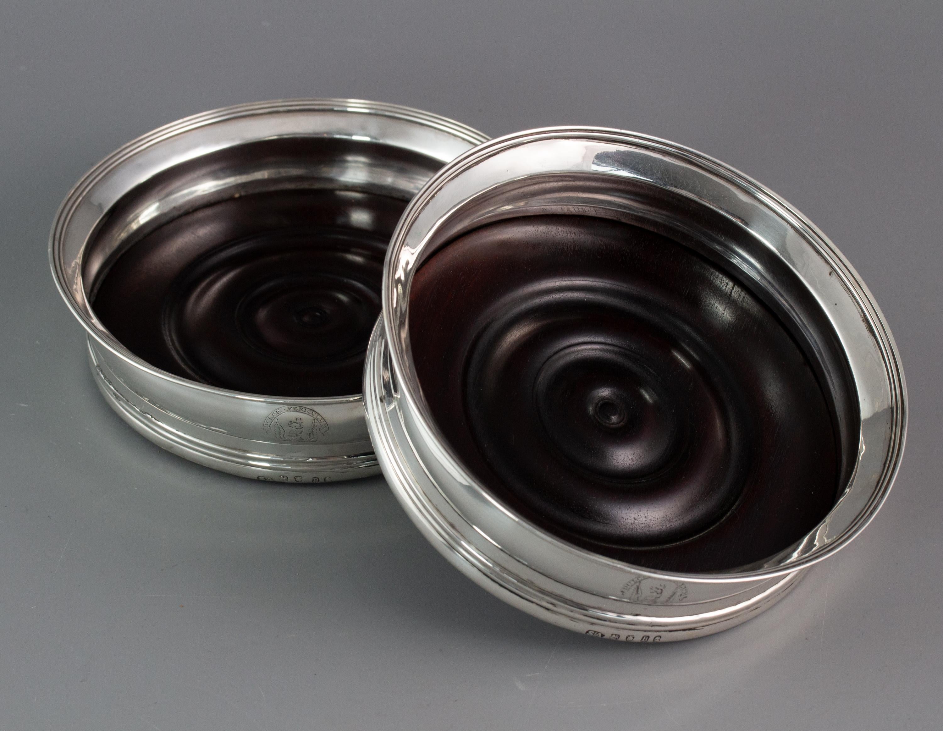 A very fine pair of George III silver wine coasters. The body of circular form with a reeded band to the base and a flared rim with a reeded border. Engraved to the side with a crest and motto “Dulce Periculum” which translates to “Danger is sweet”.