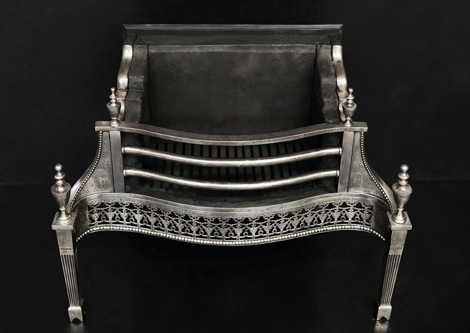 A very fine quality polished steel firegrate in the Georgian manner. The delicately pierced fret with engraving throughout, the tapering legs with flutes, engraved paterae and finials. The side wings with engraving and beading surmounted by urn