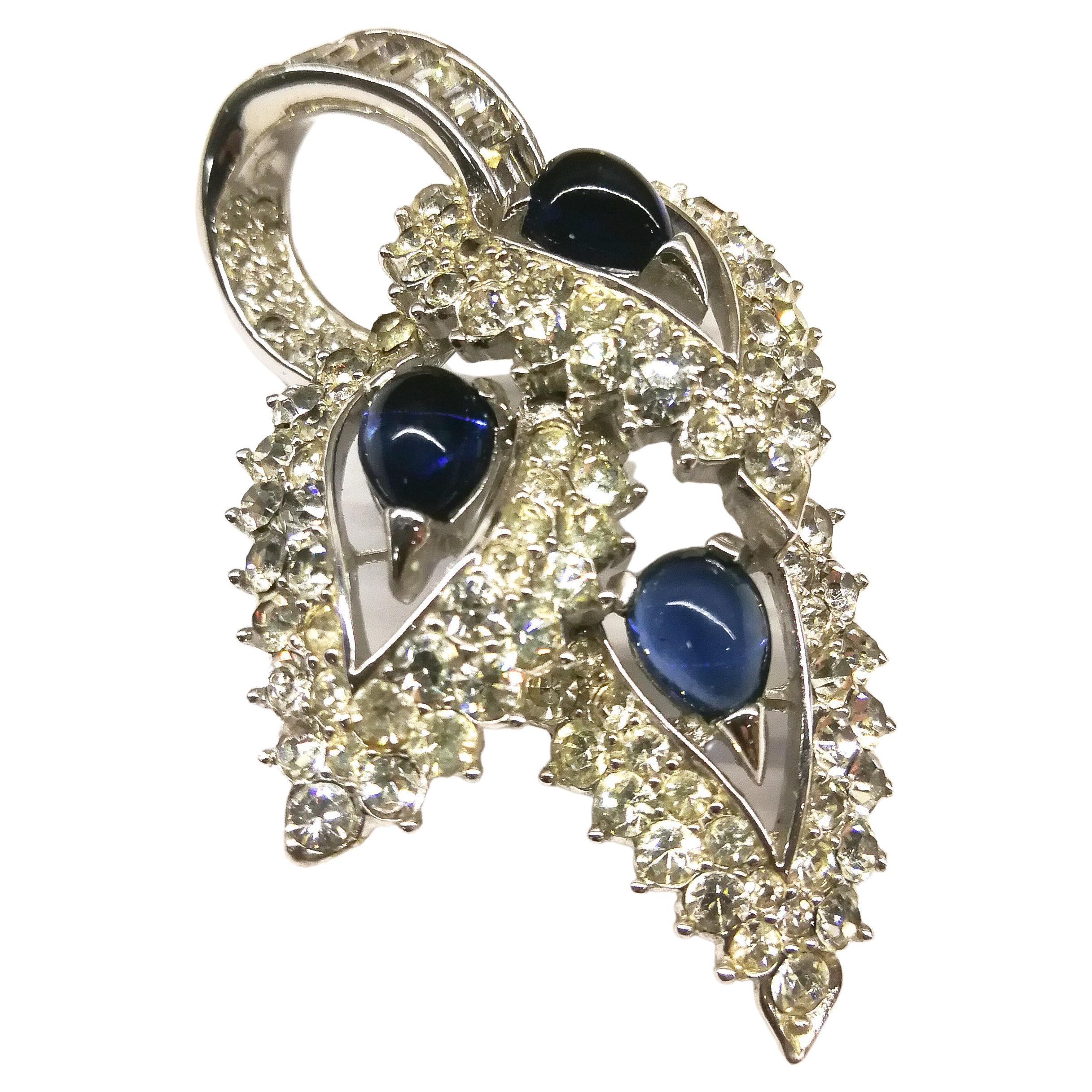 A delightful paste brooch, with a design of three stylised leaves, one on top of the other, encrusted in clear pastes and each leaf set with a sapphire blue glass cabuchon. Highly typical of the exquisite work of Marcel Boucher in the 1960s, it is a