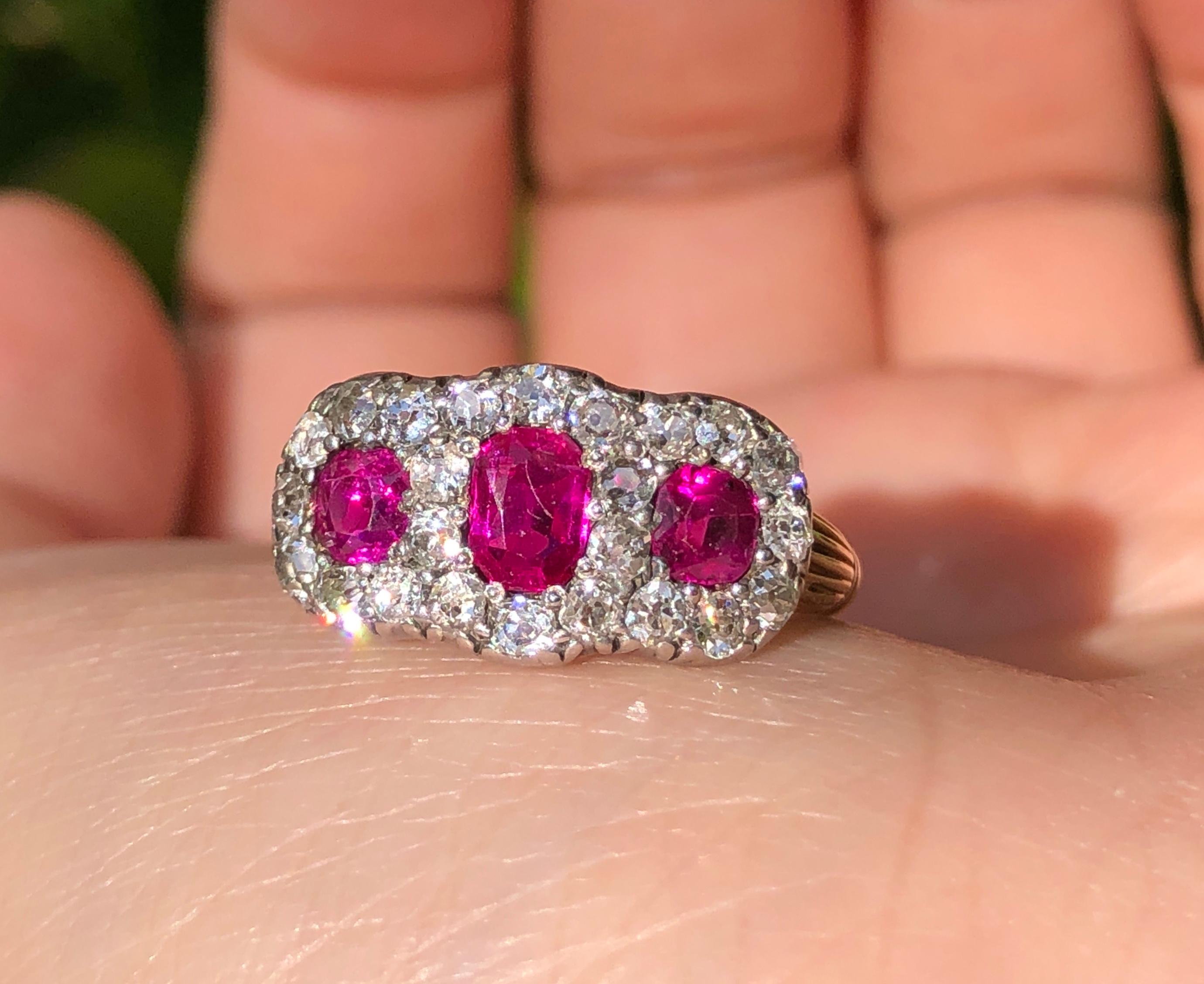 This is a very fine Victorian triple cluster ruby diamond ring. A gold and silver ring horizontally set with three oval old mine rubies in gold bead settings with an approximate total weight of 1.5 carats, encircled by cushion shaped old mine