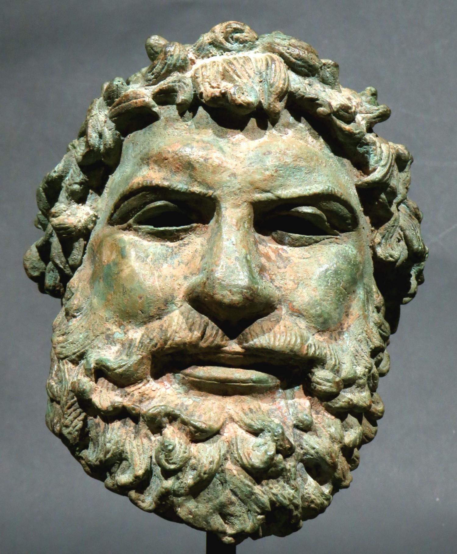 La cabeza de bronce de Zeus, finamente esculpida y patinada, muestra excelentes proporciones y rasgos hábilmente representados, con ojos perforados y cabello adornado con un Kotinos, que era una corona formada con una rama de olivo despojada que