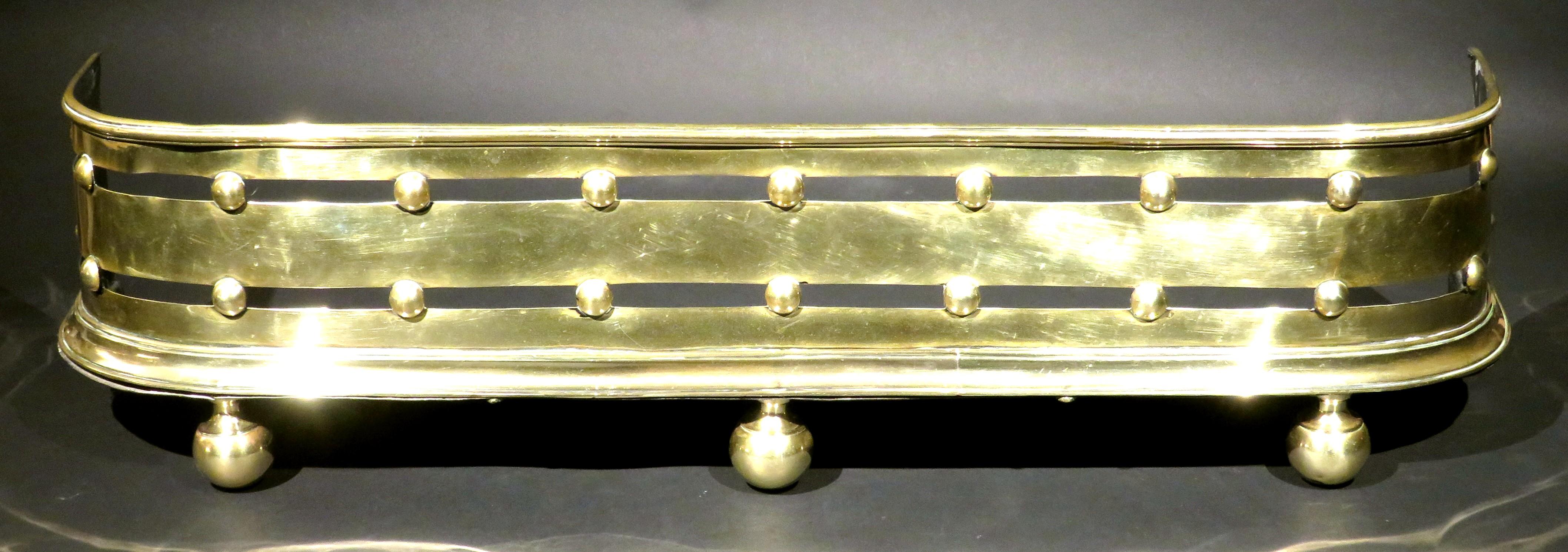 A very handsome & diminutive brass fire fender, showing a horizontal pierced panel interspersed by spherical elements, and raised overall on original ball feet.
  