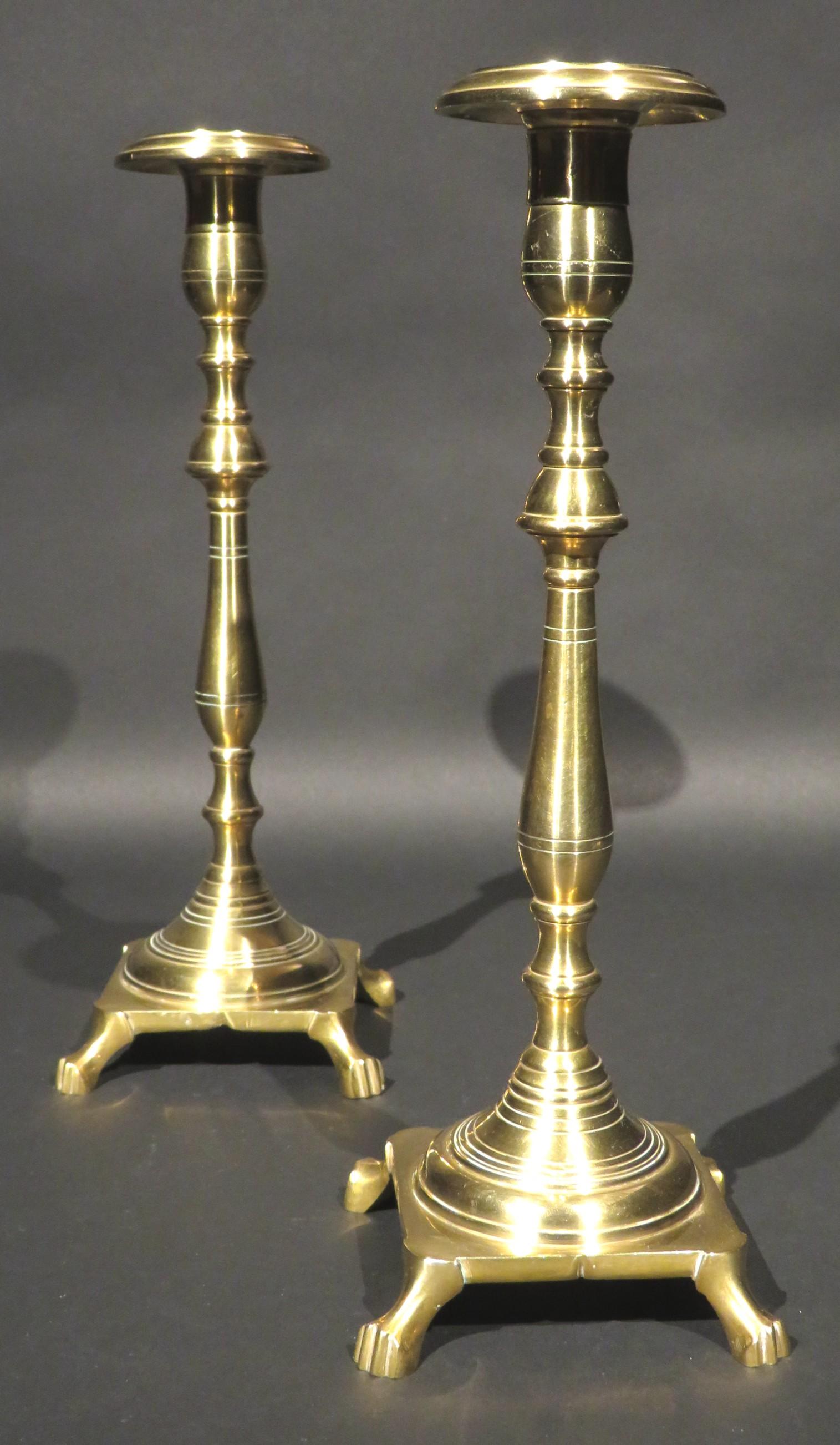 A very handsome & heavy pair of early 20th century cast brass Shabbat candlesticks. Both cast in two sections showing turned columns rising to urn-shaped nozzles with flaring drip pans, affixed to squared bases with notched decoration, raised upon
